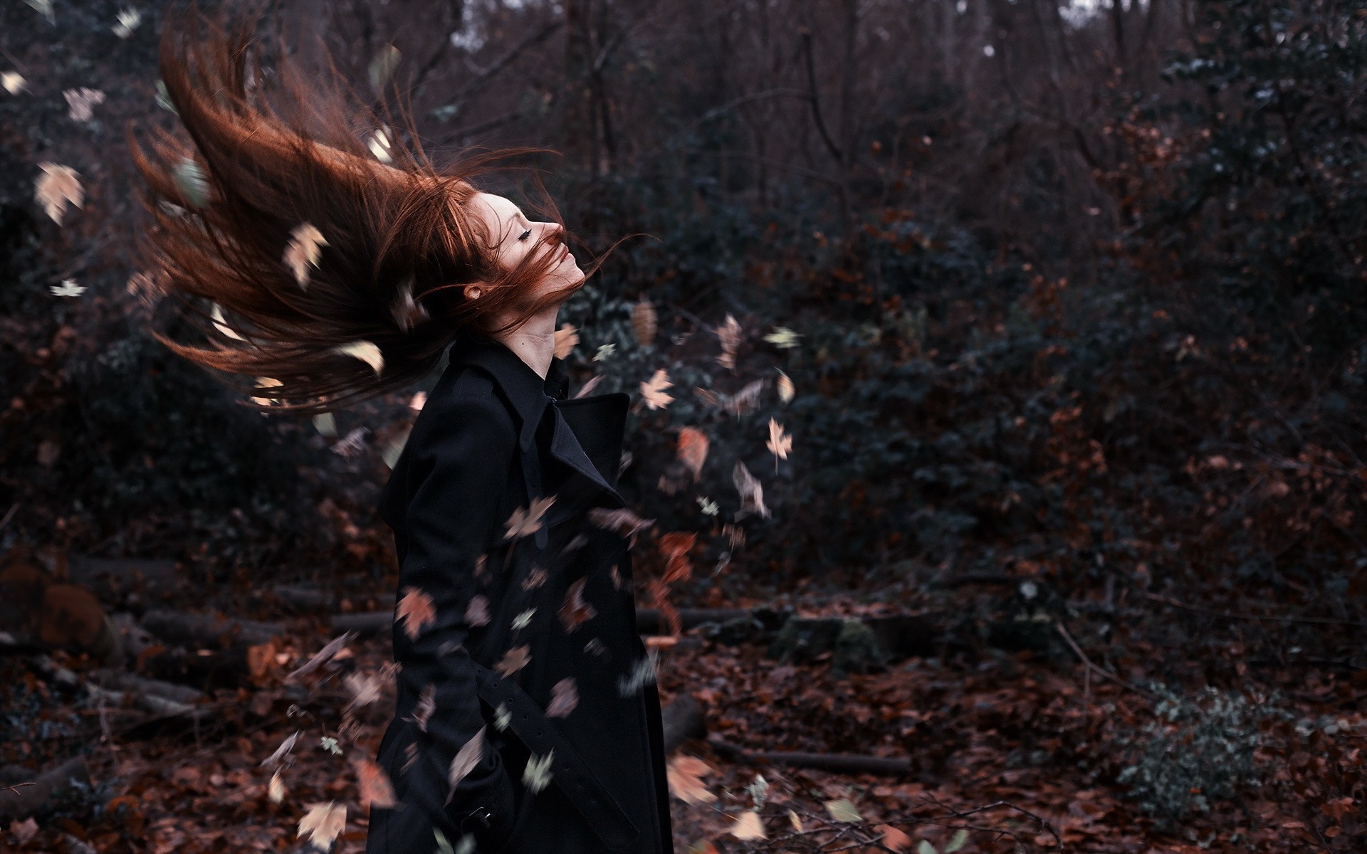 Redhead woman with long hair in a black coat in a forest with falling leaves HD Wallpaper