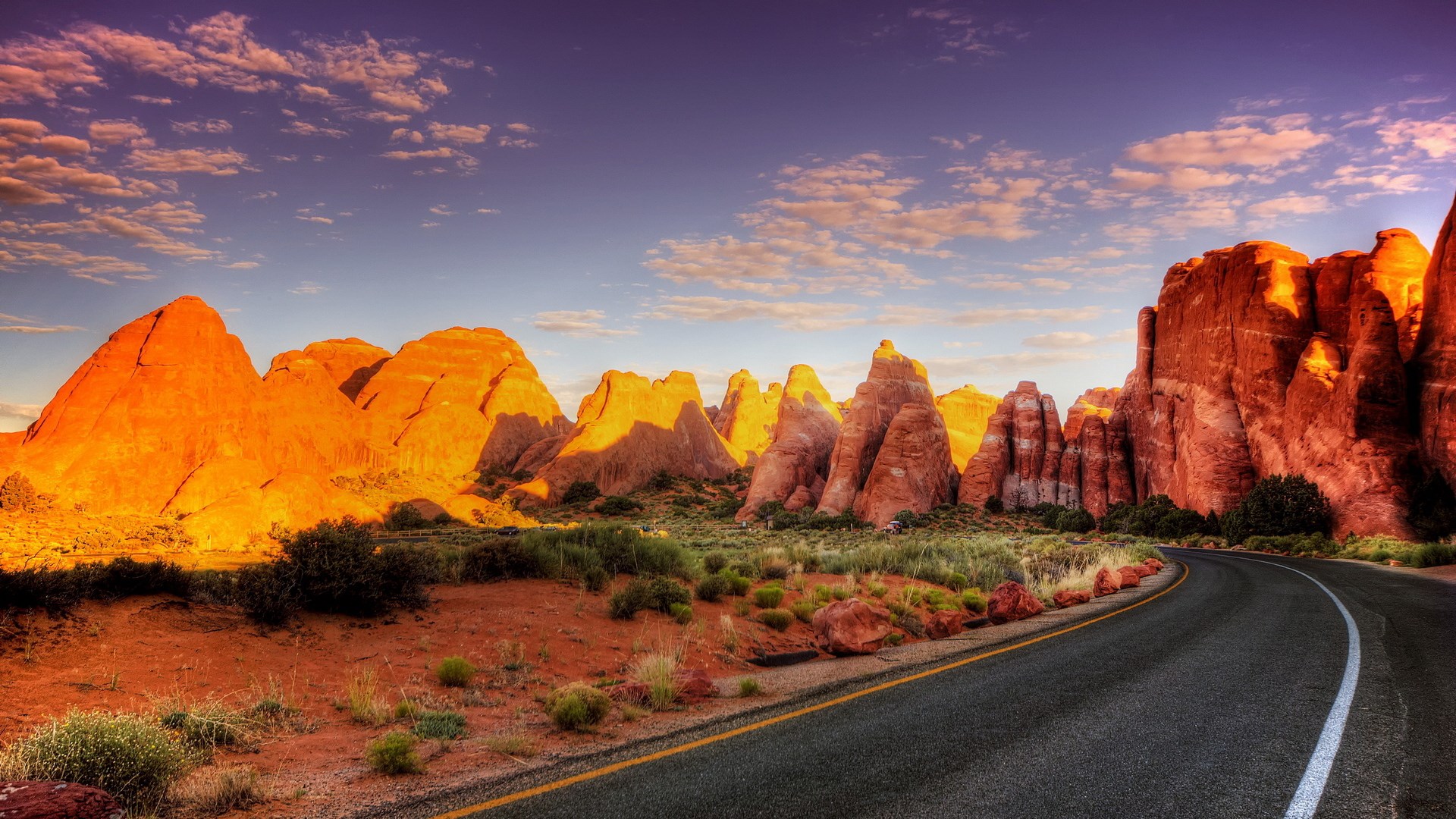 Desert road with rock formations at sunset HD Wallpaper