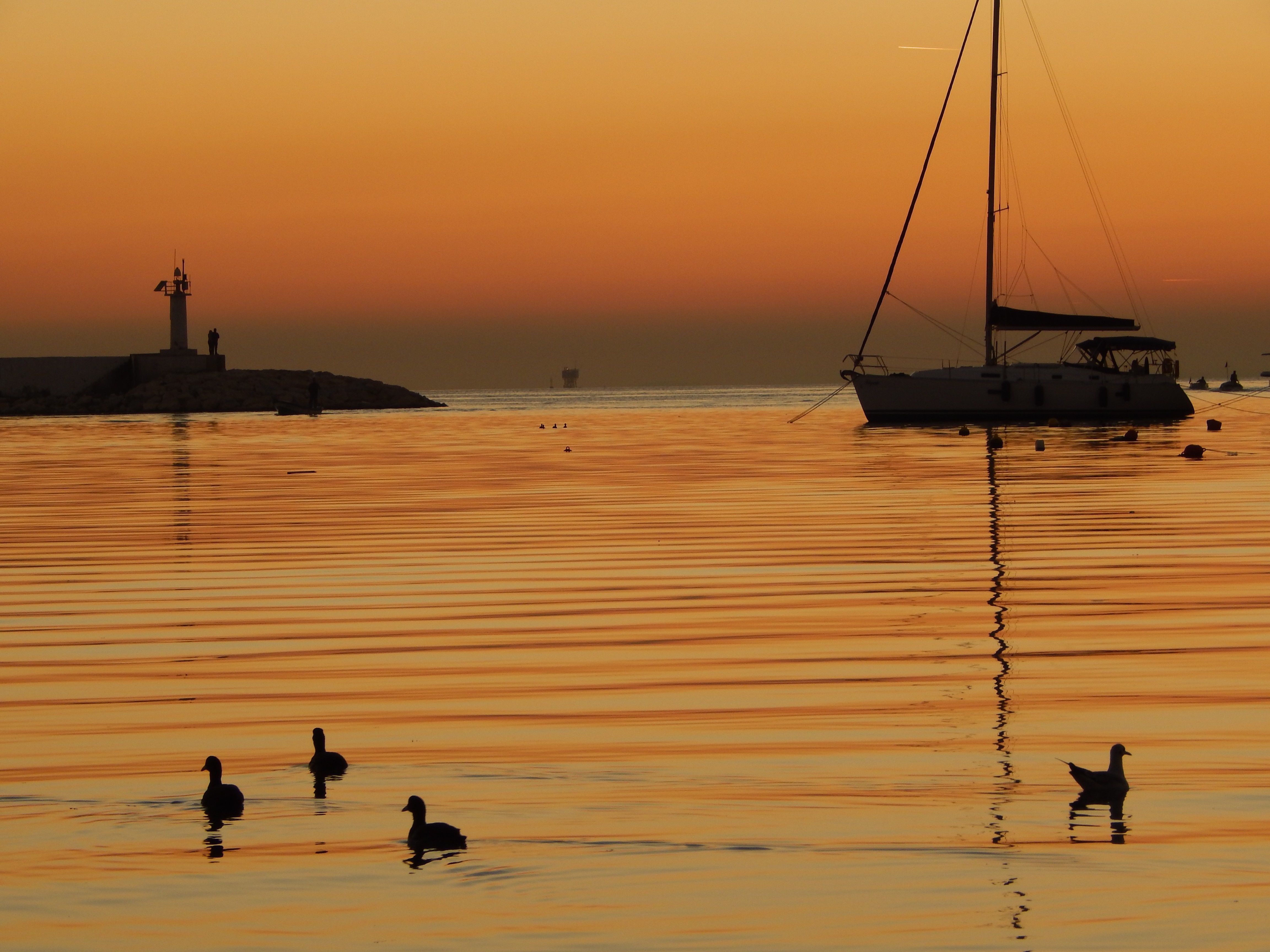 Sailboat and lighthouse at sunset over the sea HD Wallpaper