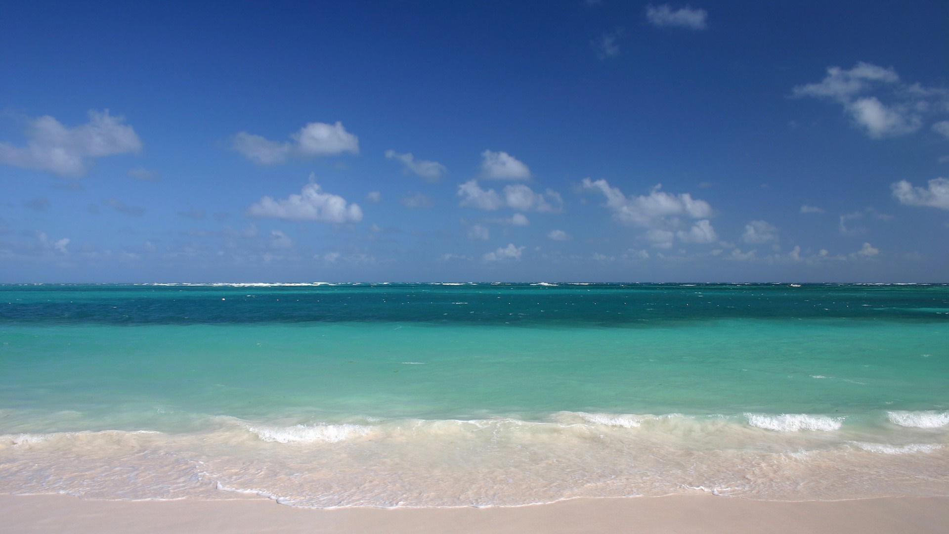Turquoise ocean waves on a sandy beach under a blue sky HD Wallpaper