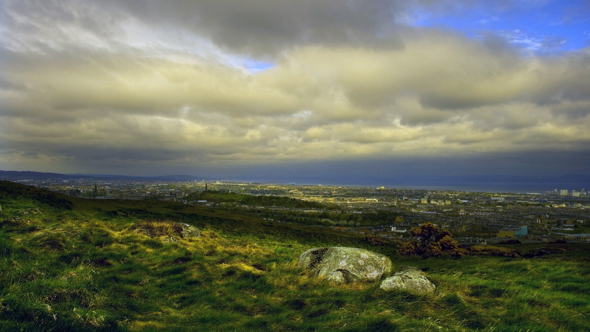 Edinburgh cityscape from a grassy hill under cloudy sky HD Wallpaper