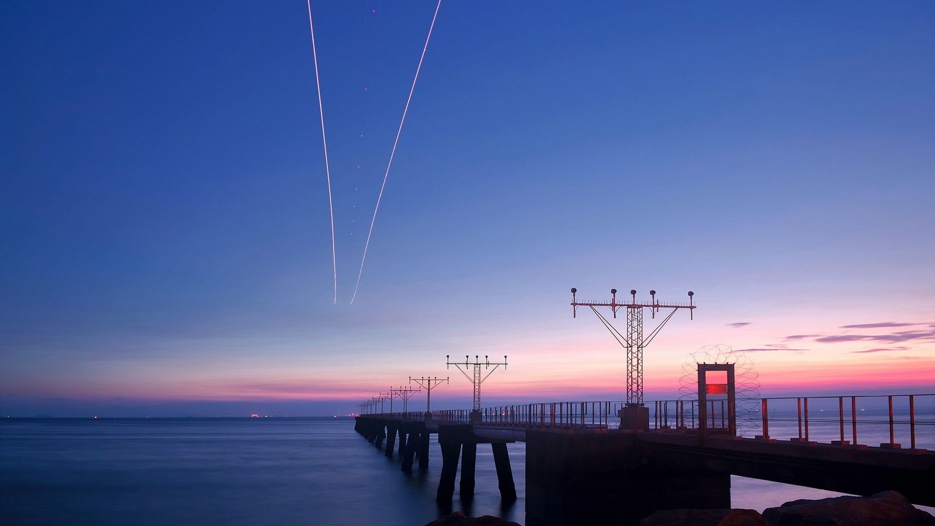 Airplane contrails over ocean pier at dusk HD Wallpaper