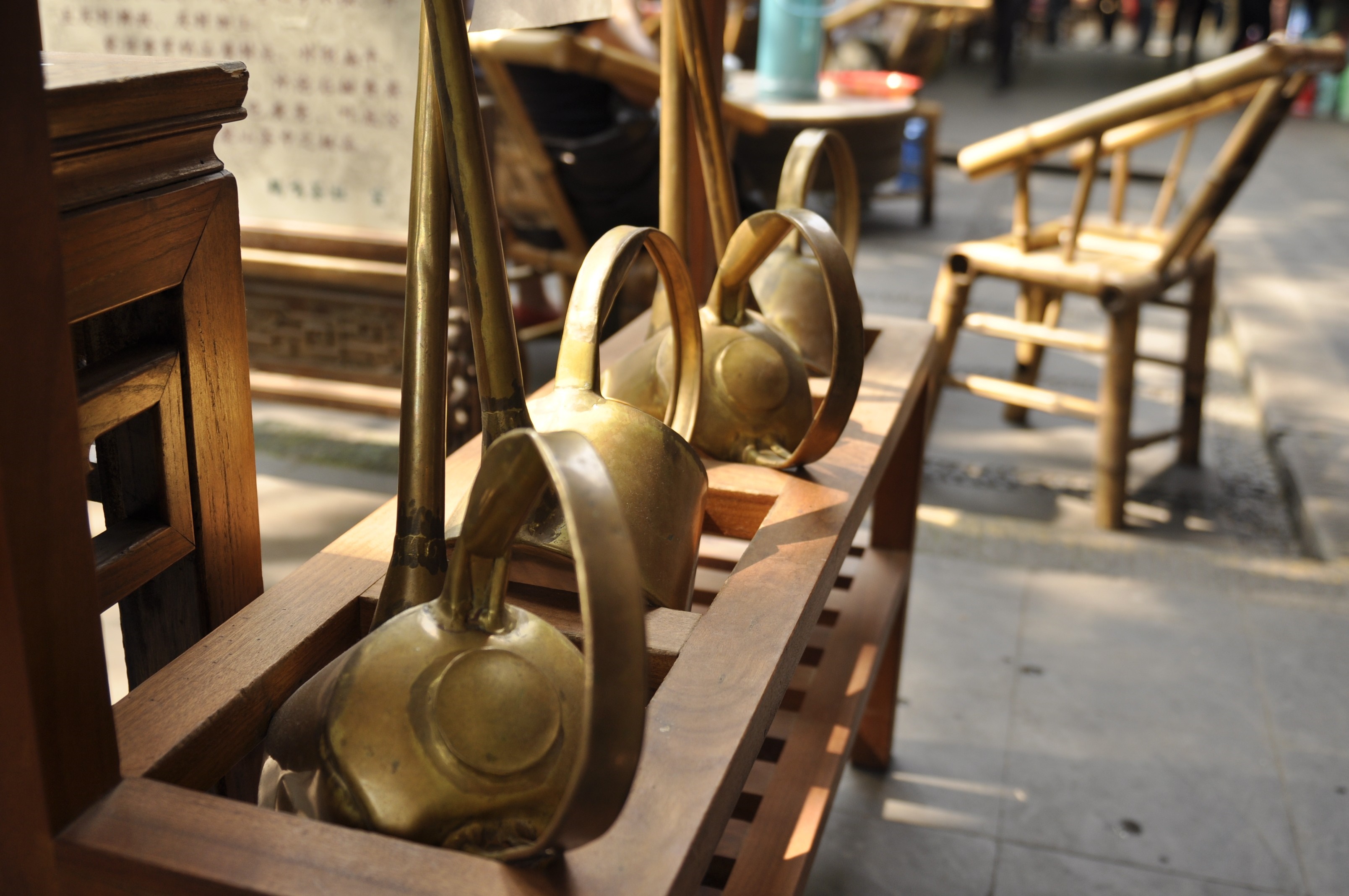 Brass watering cans on a wooden shelf with a bamboo chair HD Wallpaper