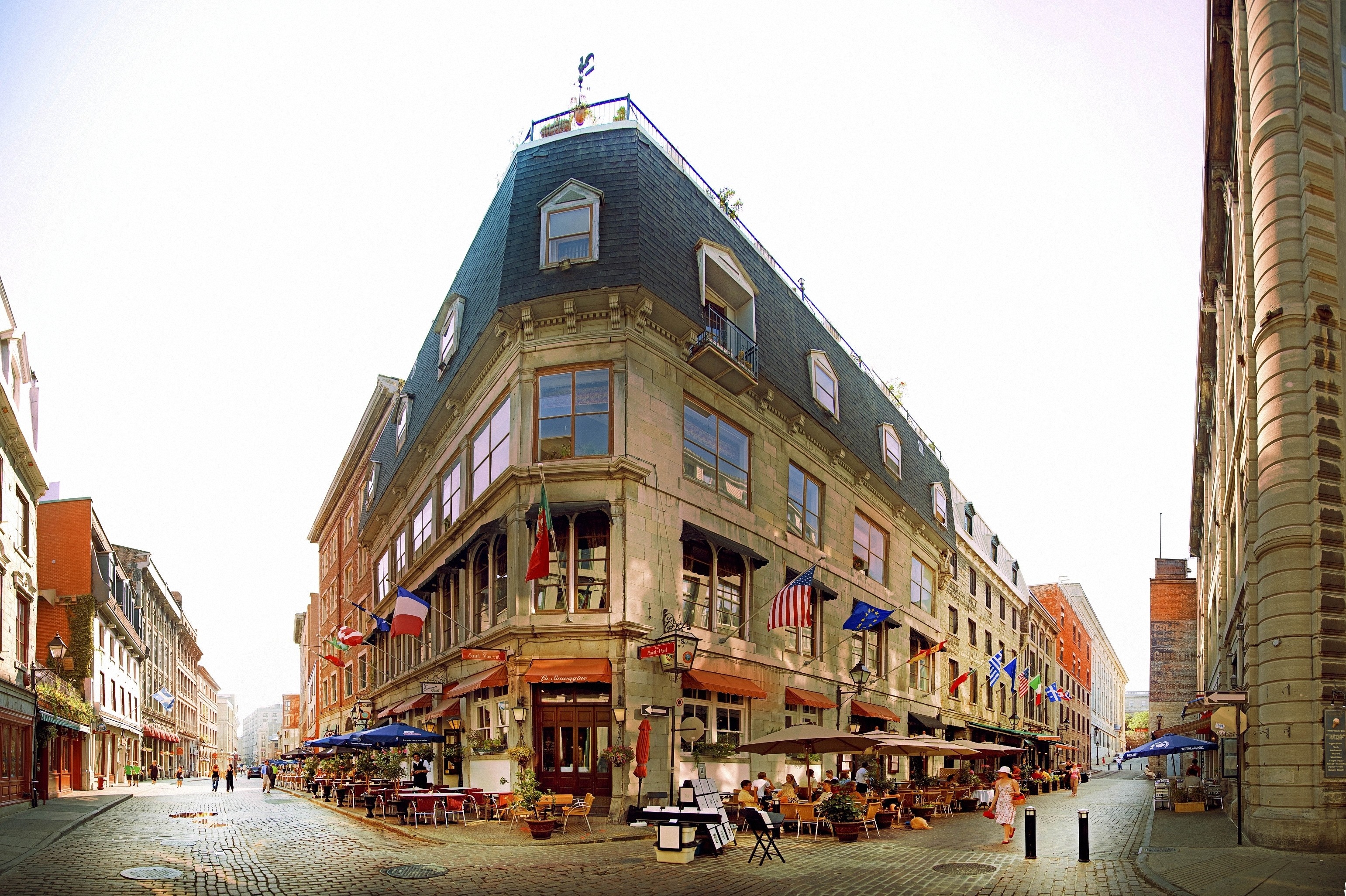 Corner building with outdoor cafe on cobblestone street HD Wallpaper