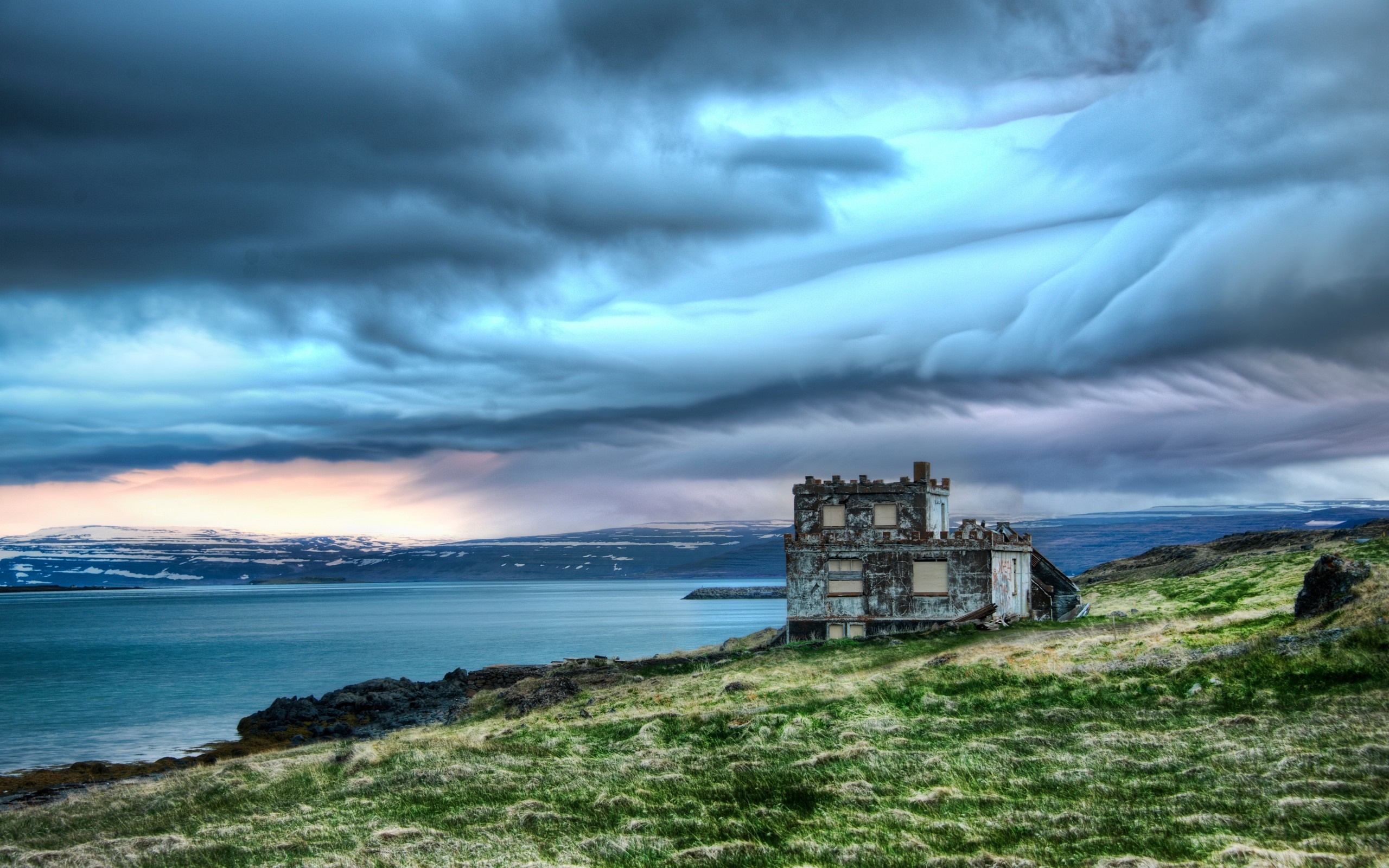 Abandoned building on a grassy coast under stormy clouds HD Wallpaper