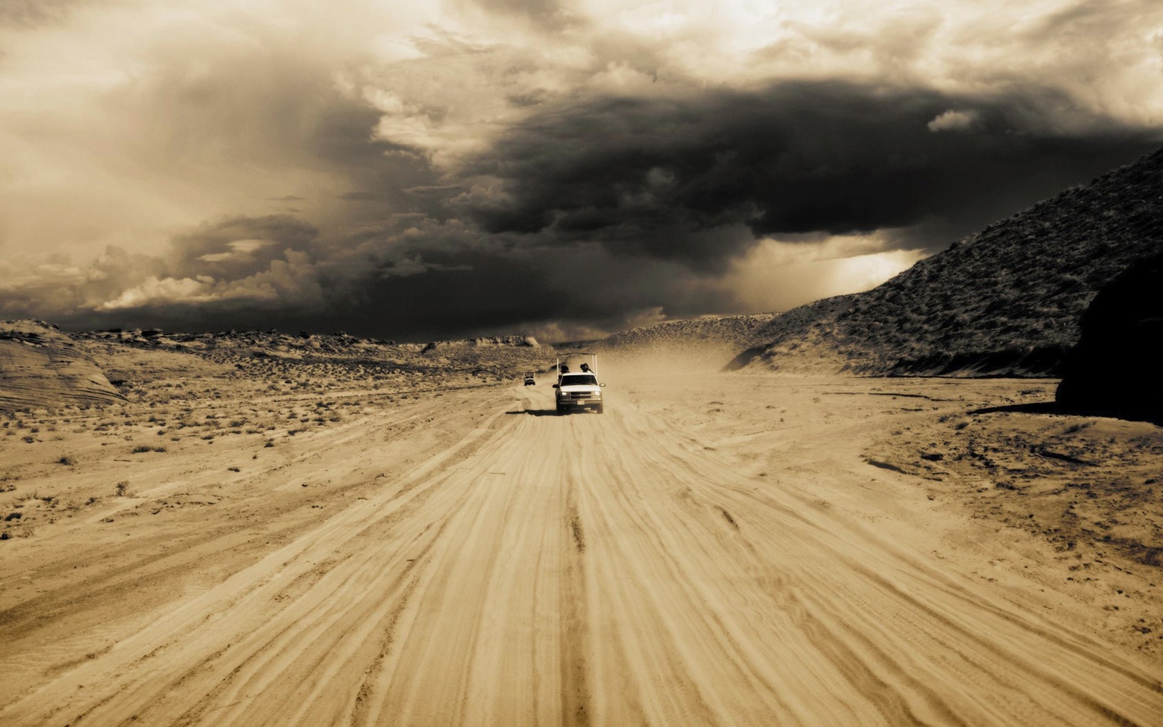 Two cars driving on a dusty road in a desert landscape under stormy clouds HD Wallpaper