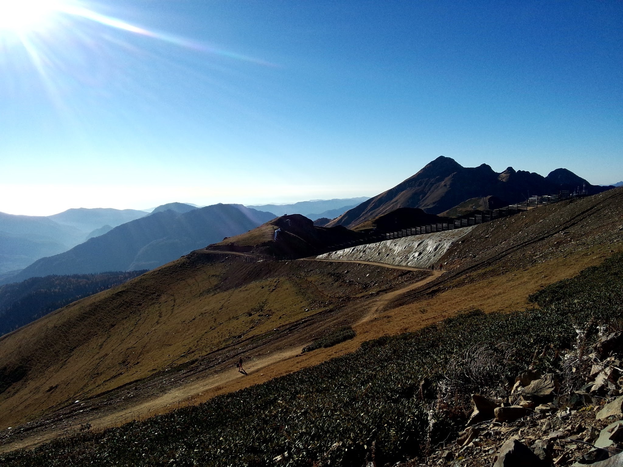 Mountain range with sunlit sky and hiking path HD Wallpaper