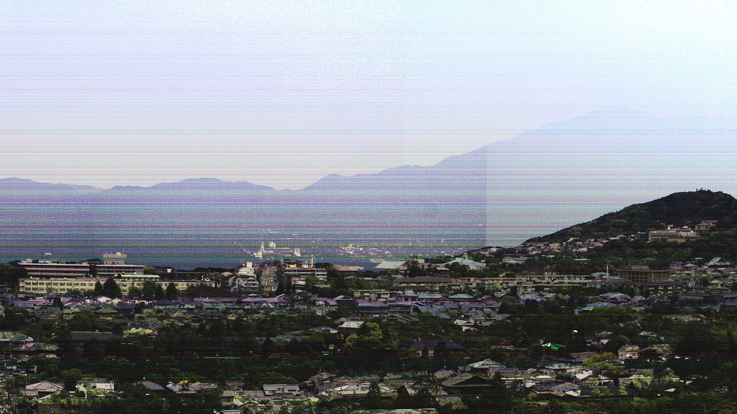 Cityscape with mountains and sea under a hazy sky HD Wallpaper