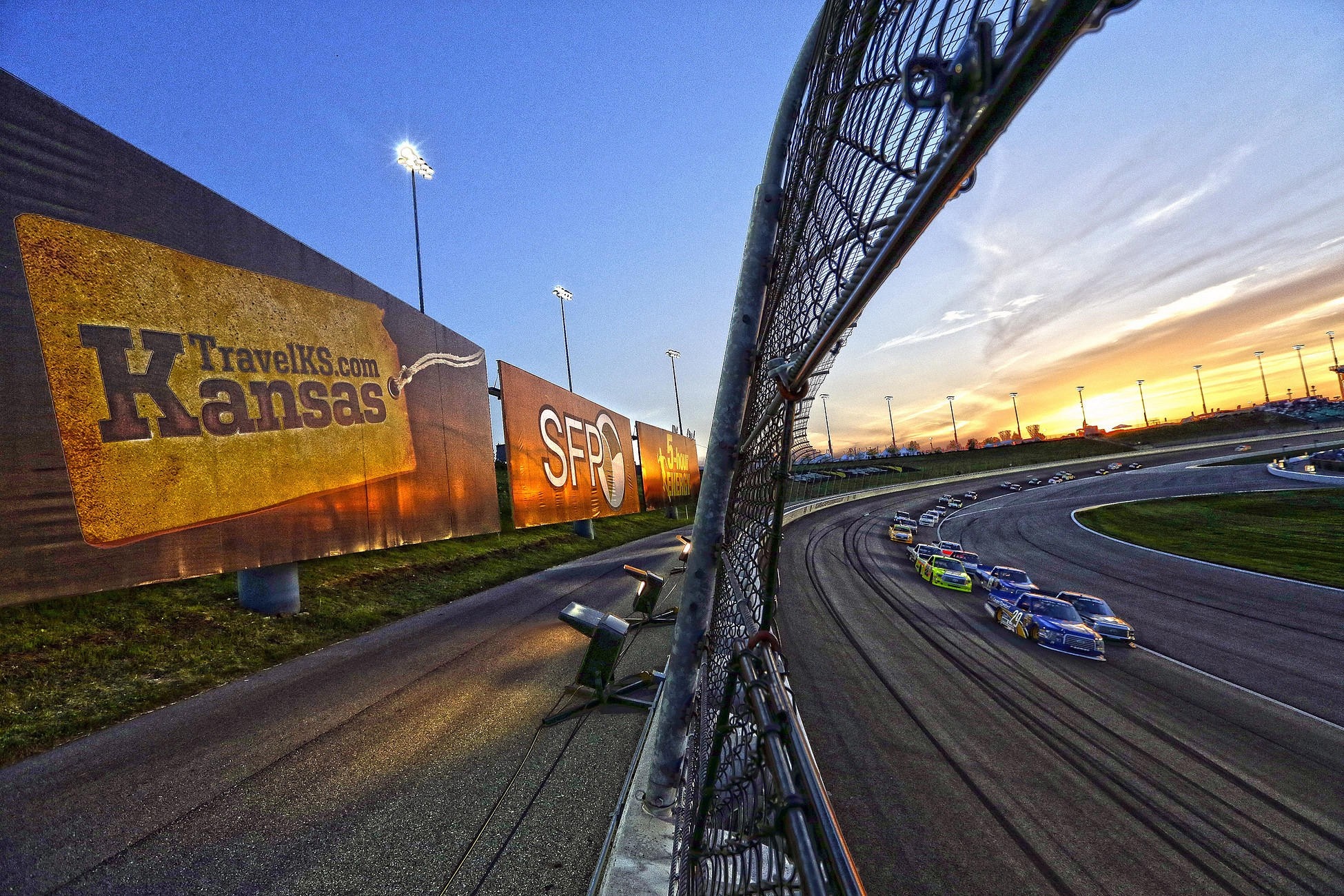 Race cars on a track at sunset with billboards HD Wallpaper