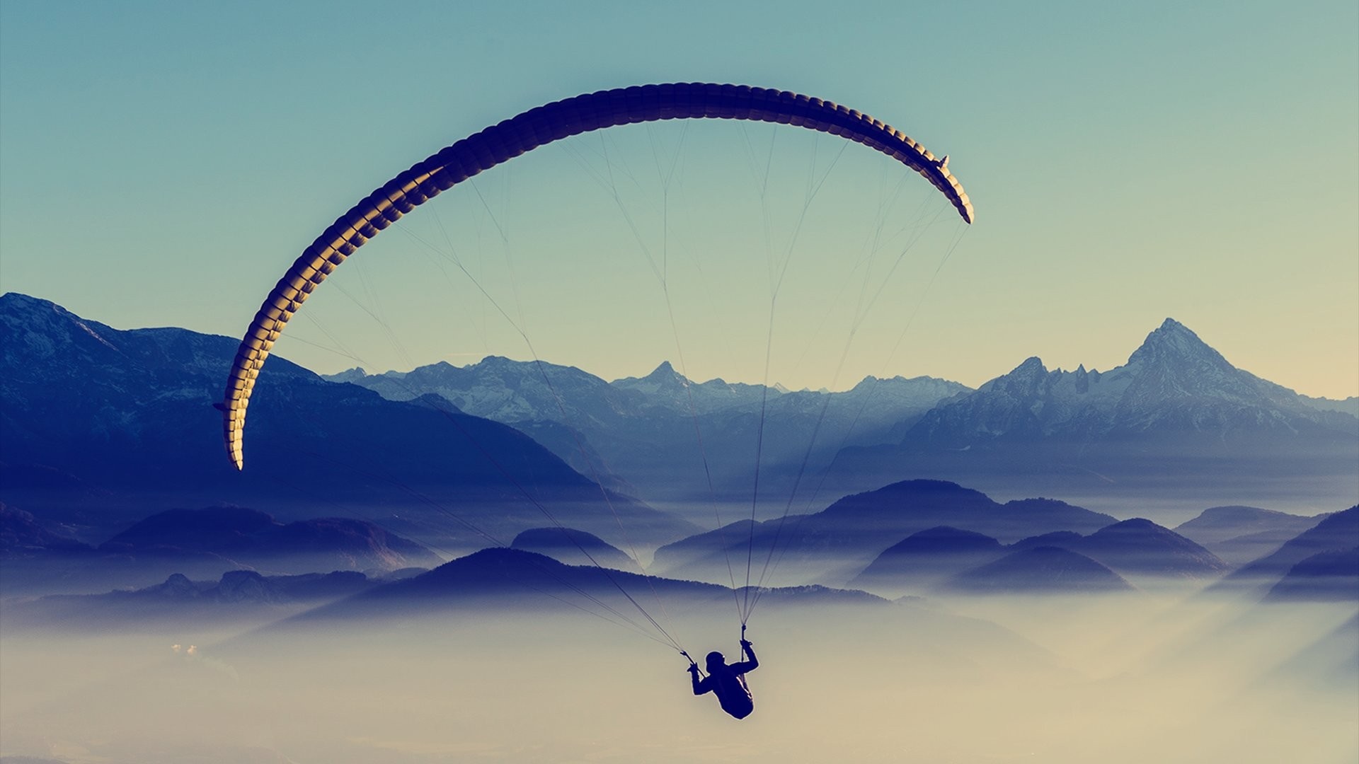 Paraglider flying over misty mountains at sunrise HD Wallpaper