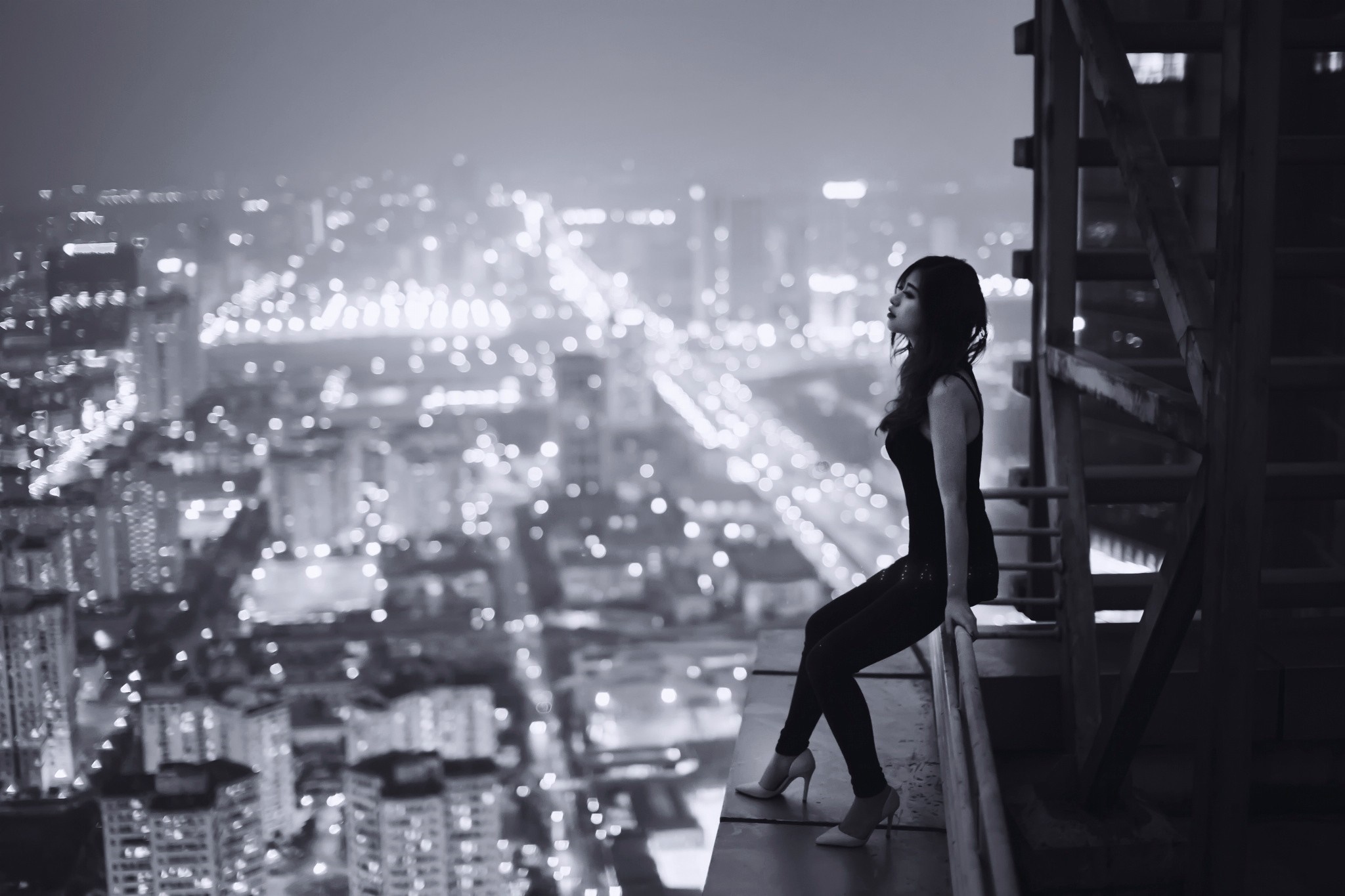 Woman sitting on edge of skyscraper overlooking city at night HD Wallpaper
