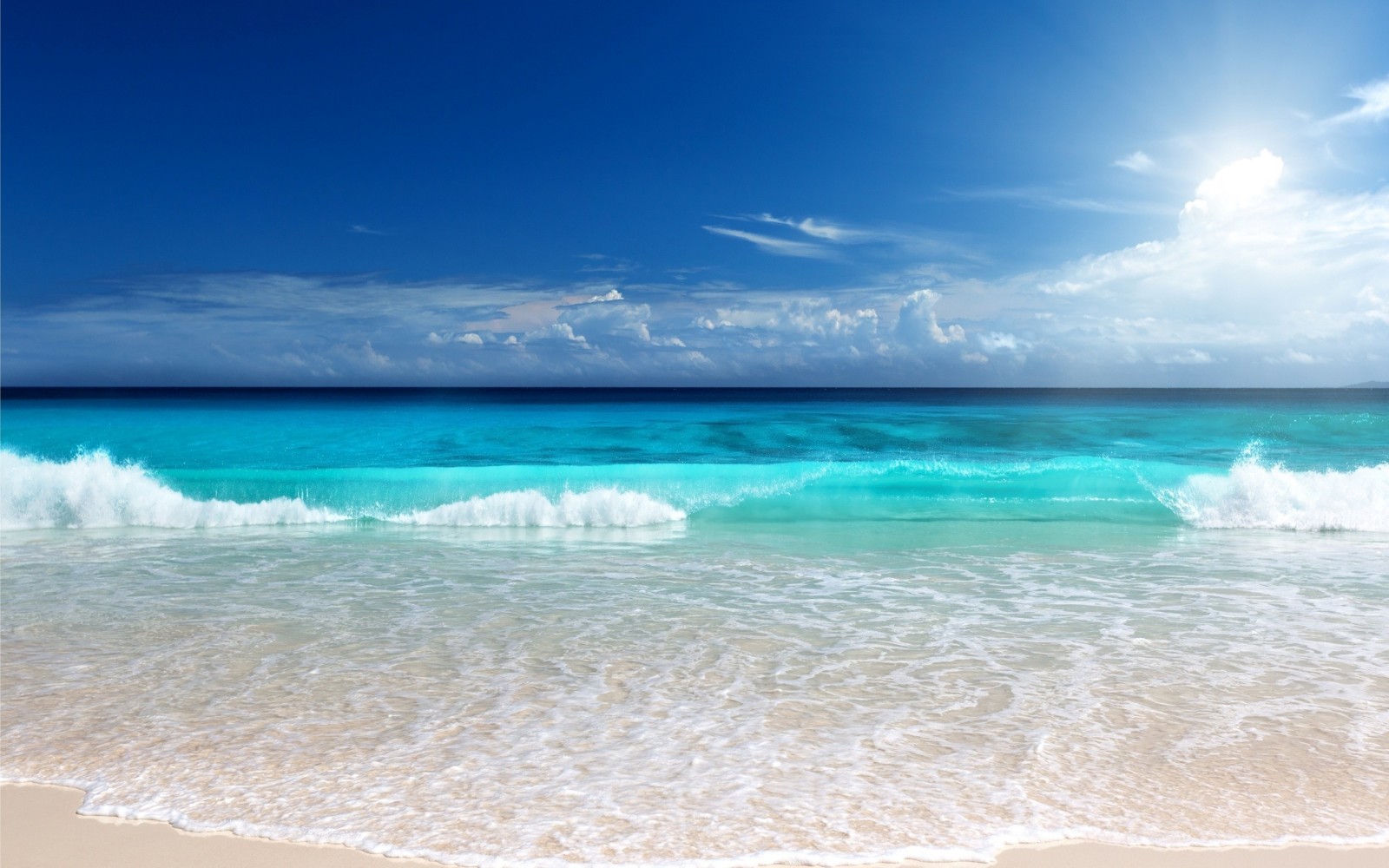 Turquoise ocean waves crash on a sandy beach under a blue sky HD Wallpaper