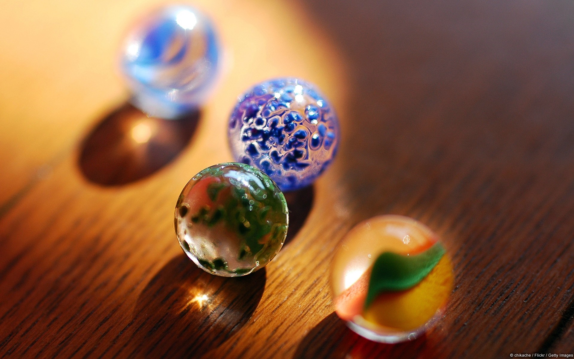Four colorful glass marbles on a wooden surface HD Wallpaper