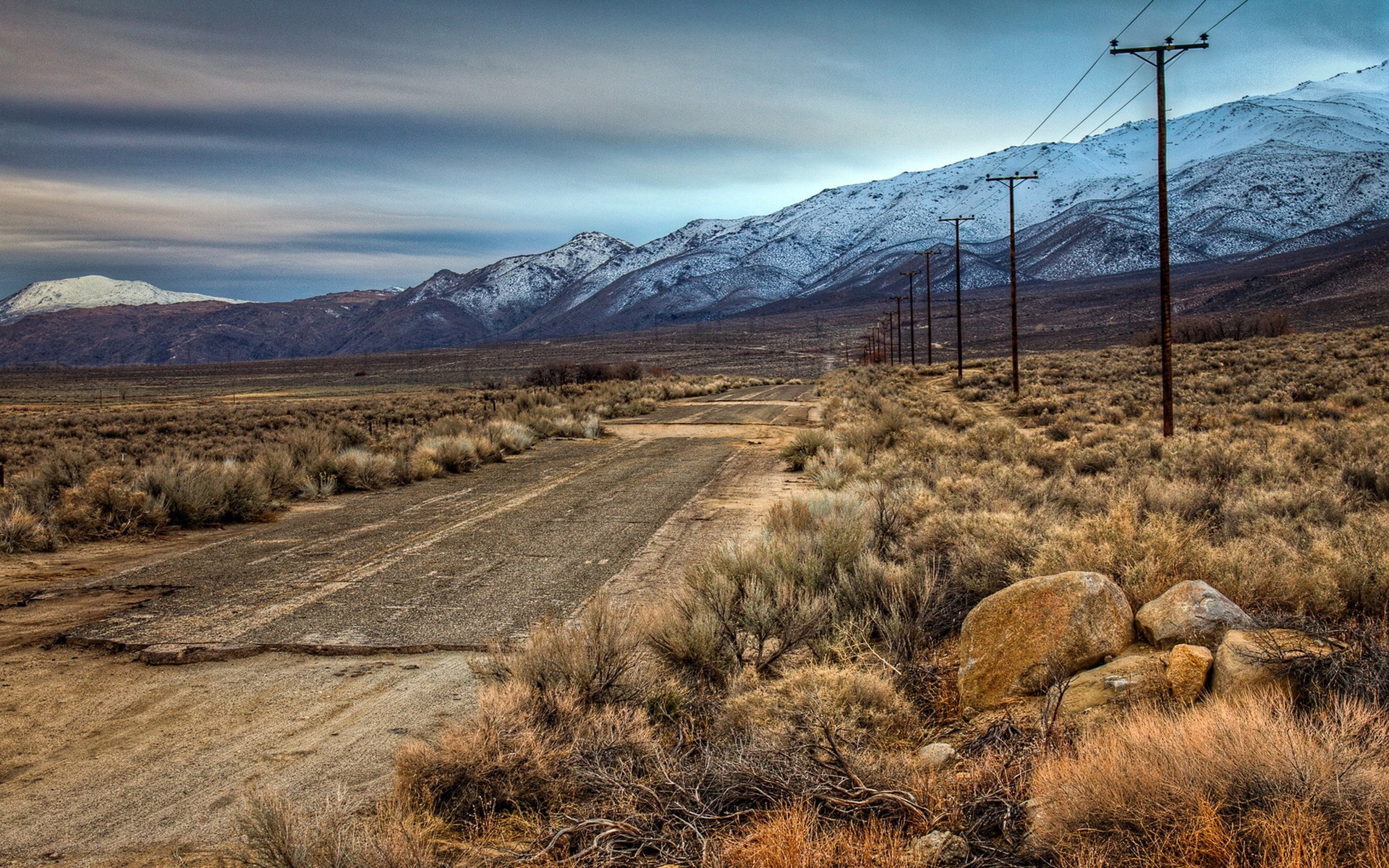 Abandoned road leading to snow-capped mountains with power lines HD Wallpaper
