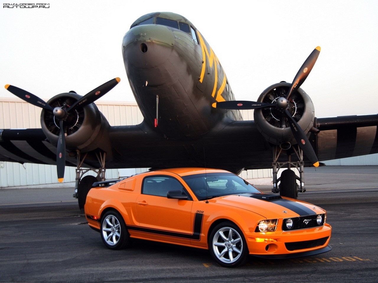 Orange Ford Mustang parked in front of a vintage airplane HD Wallpaper