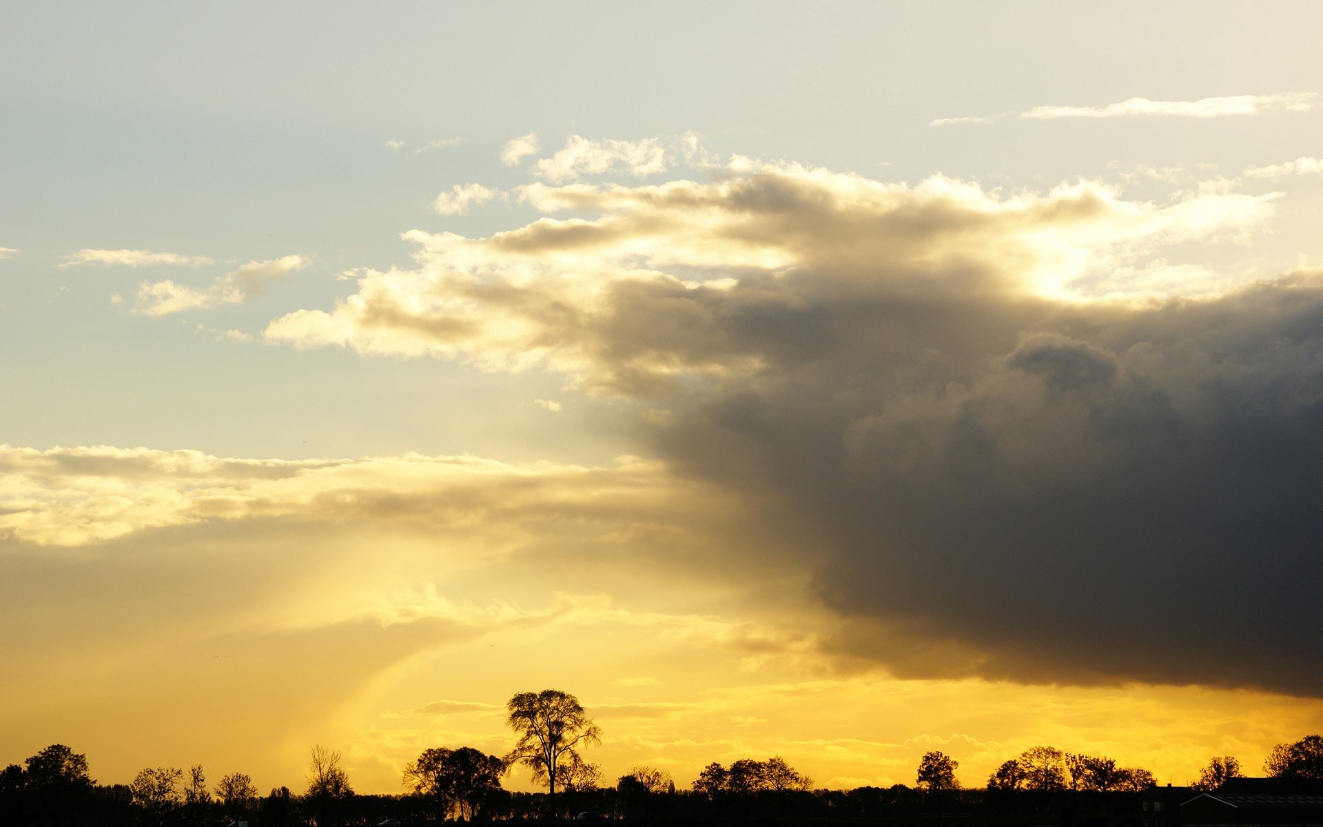 Sunset clouds over silhouetted trees and landscape HD Wallpaper