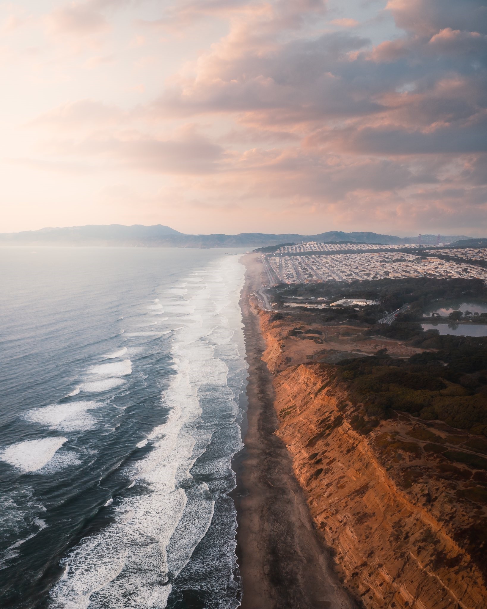 Ocean waves crash on a sandy beach with cliffs HD Phone Wallpaper