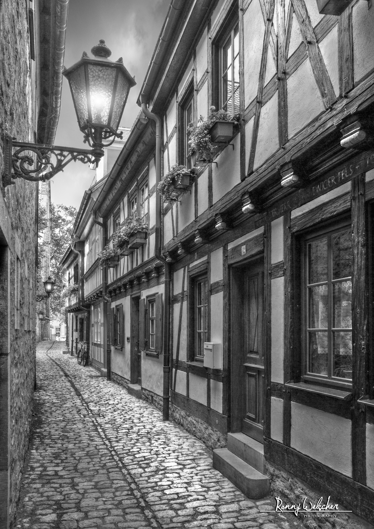 Cobblestone alley with historic timber-framed buildings and street lamp HD Phone Wallpaper