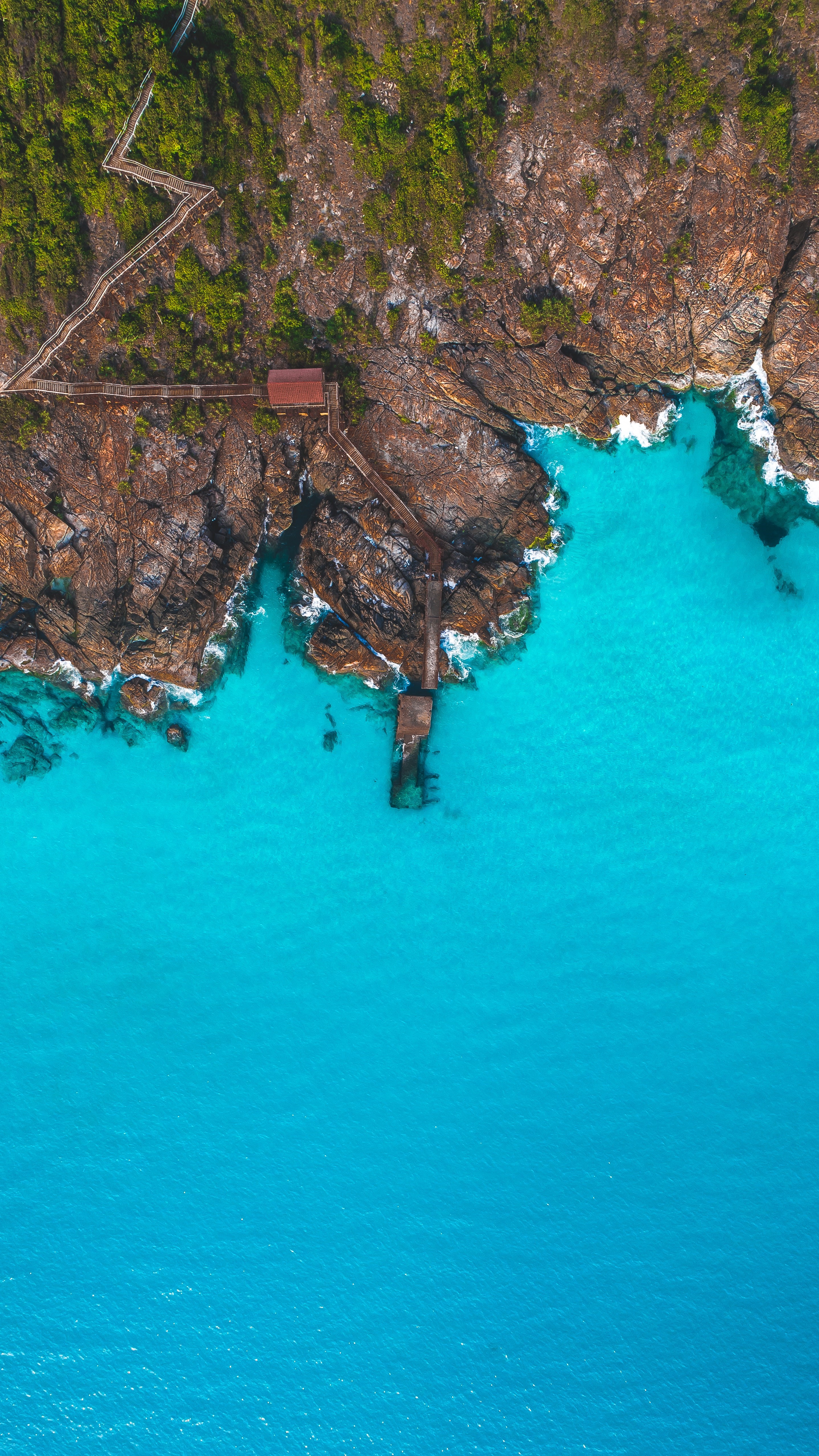Aerial view of a wooden pier and rocky coast with turquoise water HD Phone Wallpaper