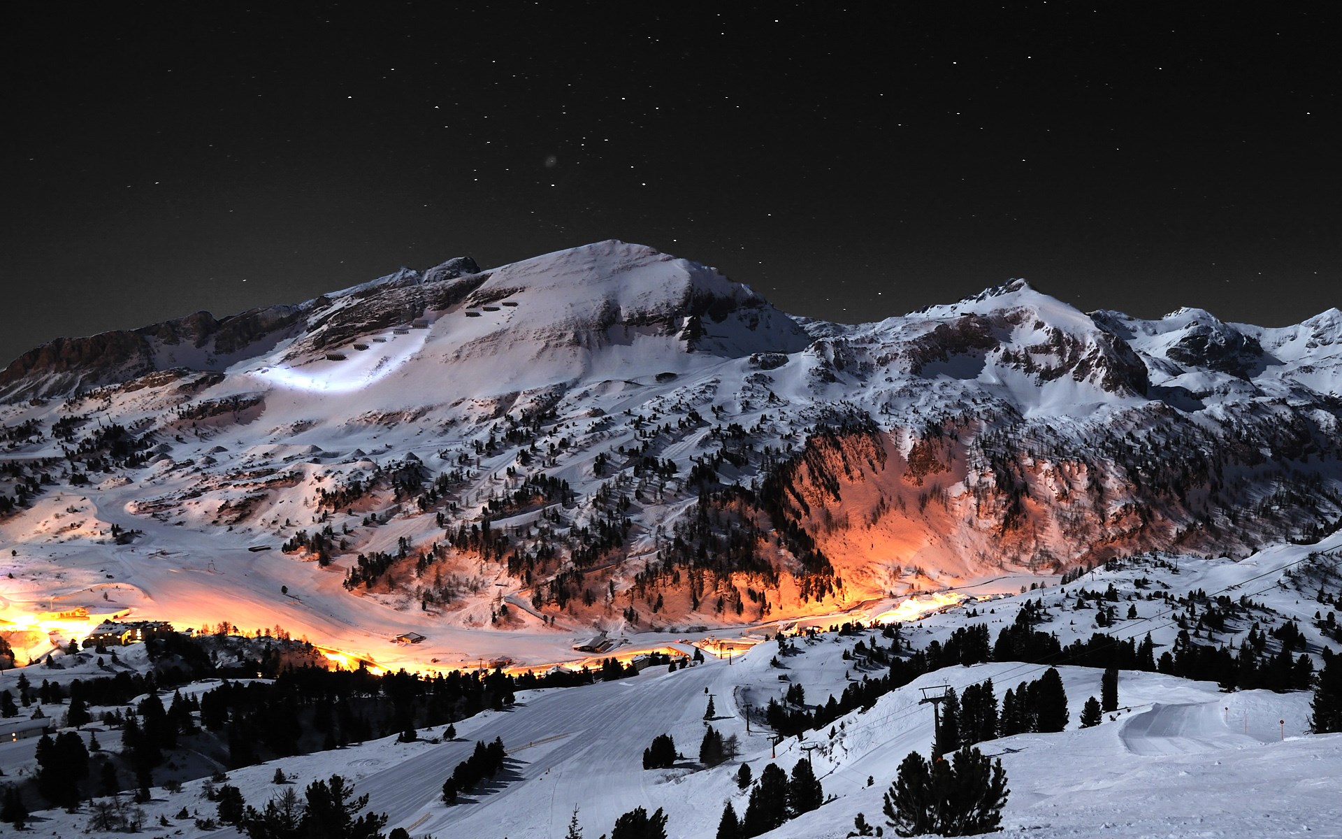 Snowy mountains at night with village lights HD Wallpaper