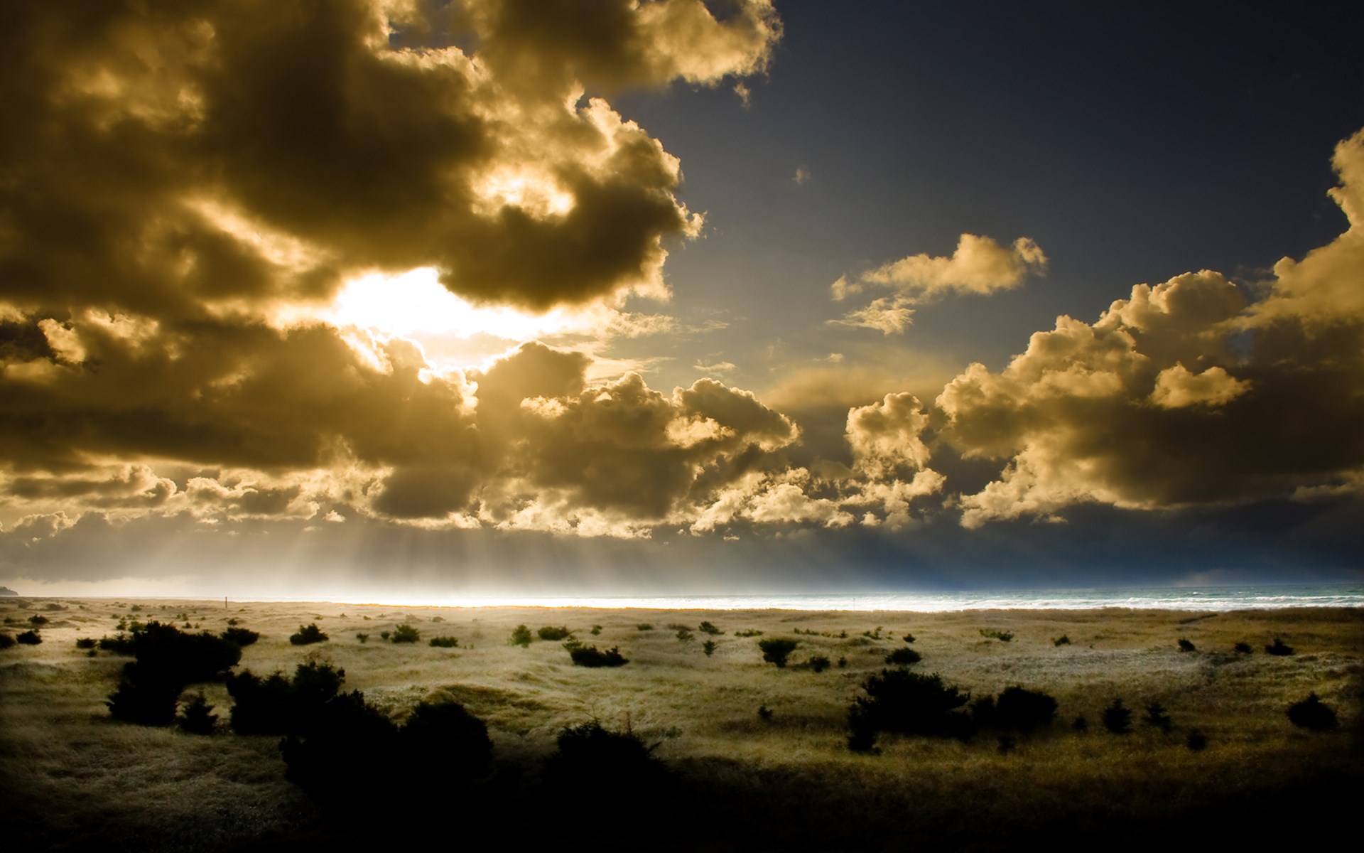 Sunlight breaking through dramatic clouds over a coastal landscape HD Wallpaper