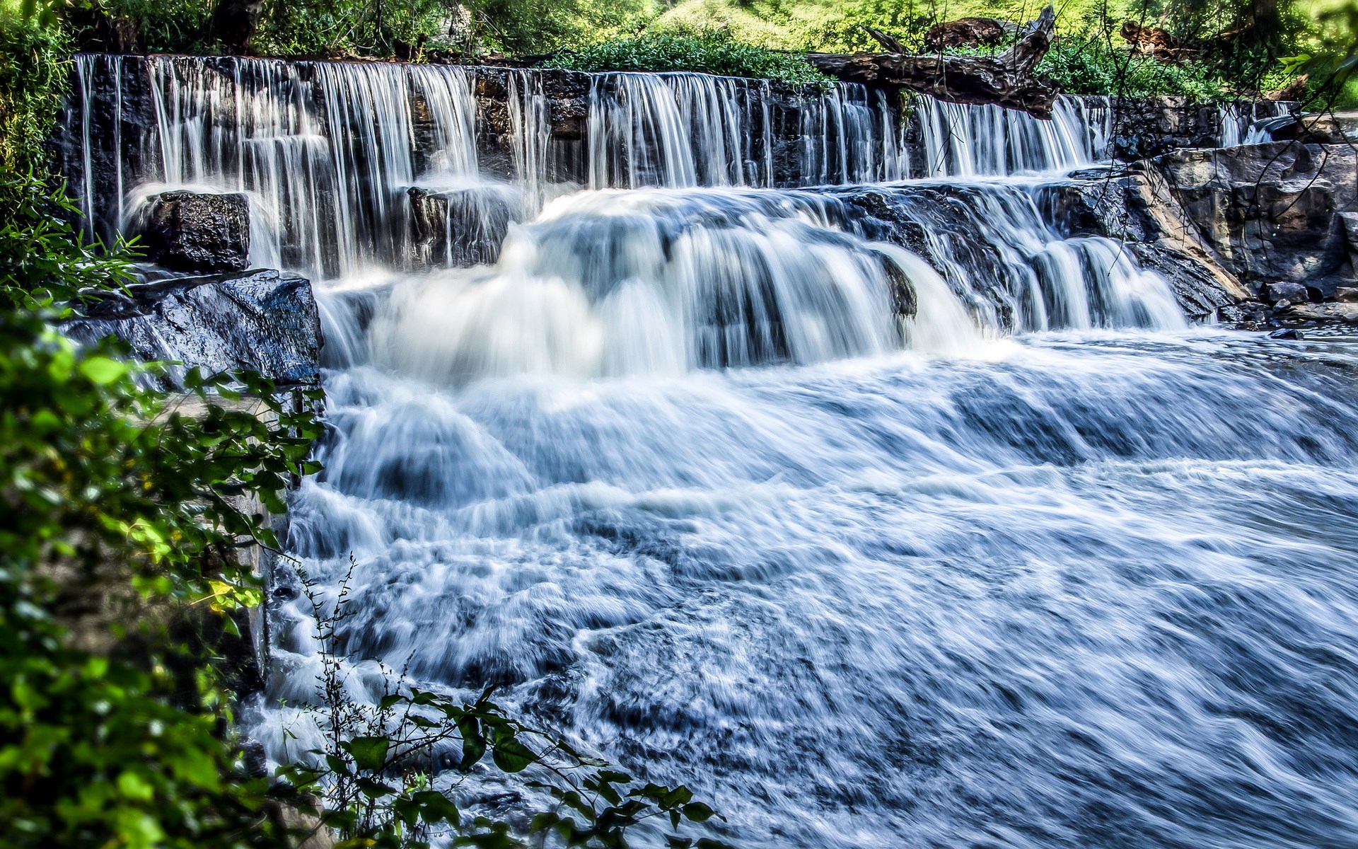 Waterfall cascading over rocks with lush green foliage HD Wallpaper