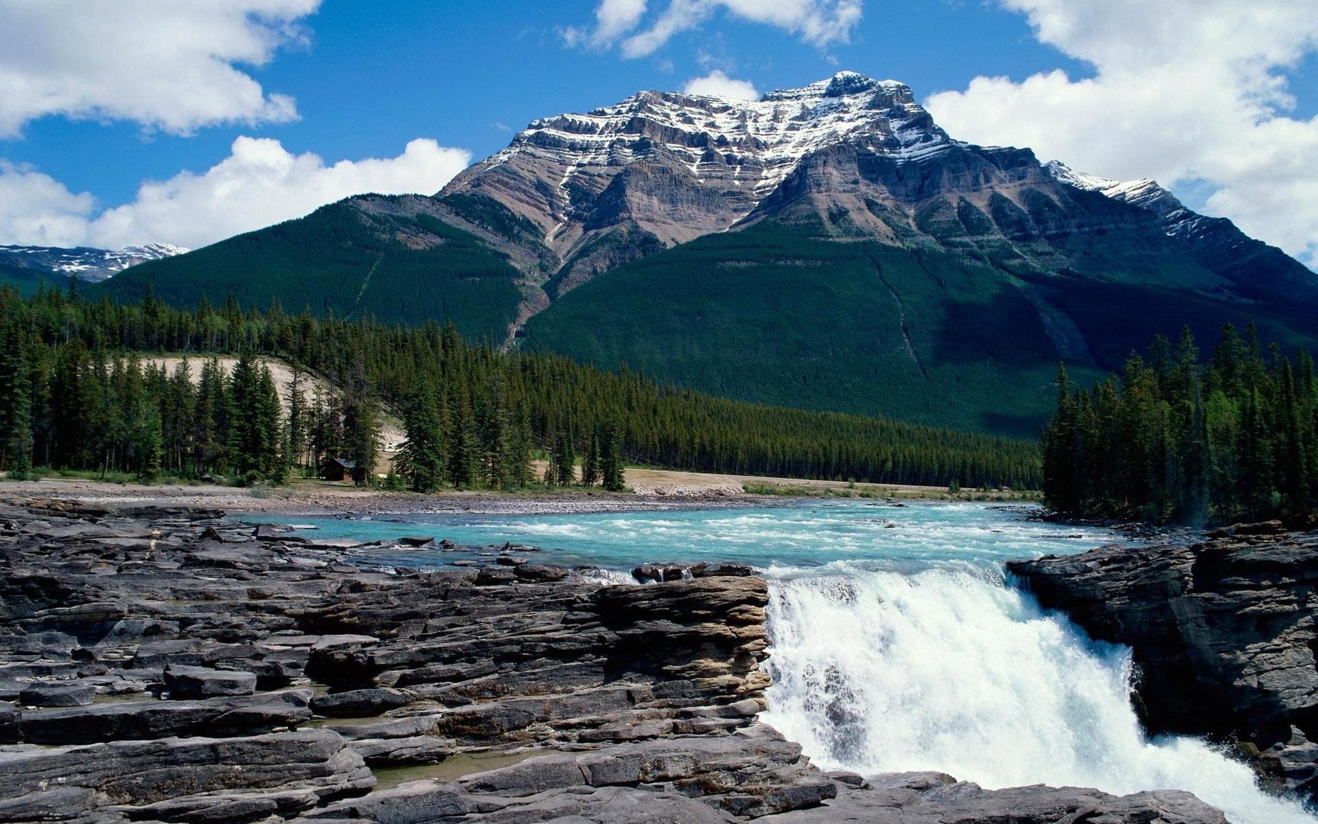 Waterfall flowing over rocks with a mountain and forest background HD Wallpaper