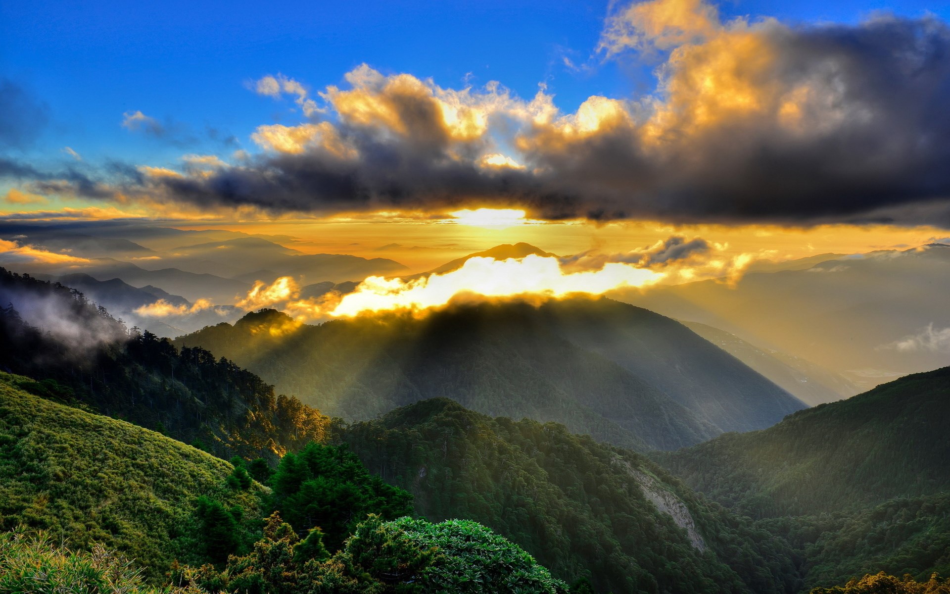 Sunlight breaking through clouds over misty mountains HD Wallpaper