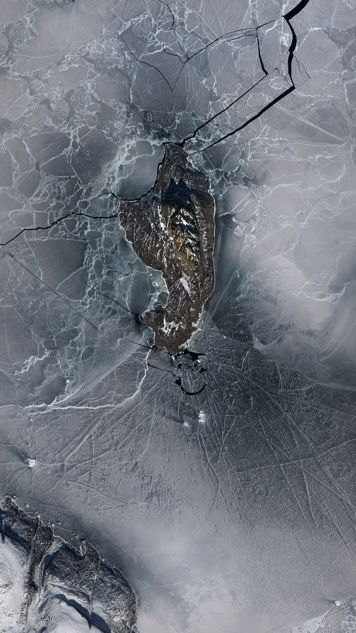 Aerial view of a rocky island surrounded by cracked ice HD Phone Wallpaper