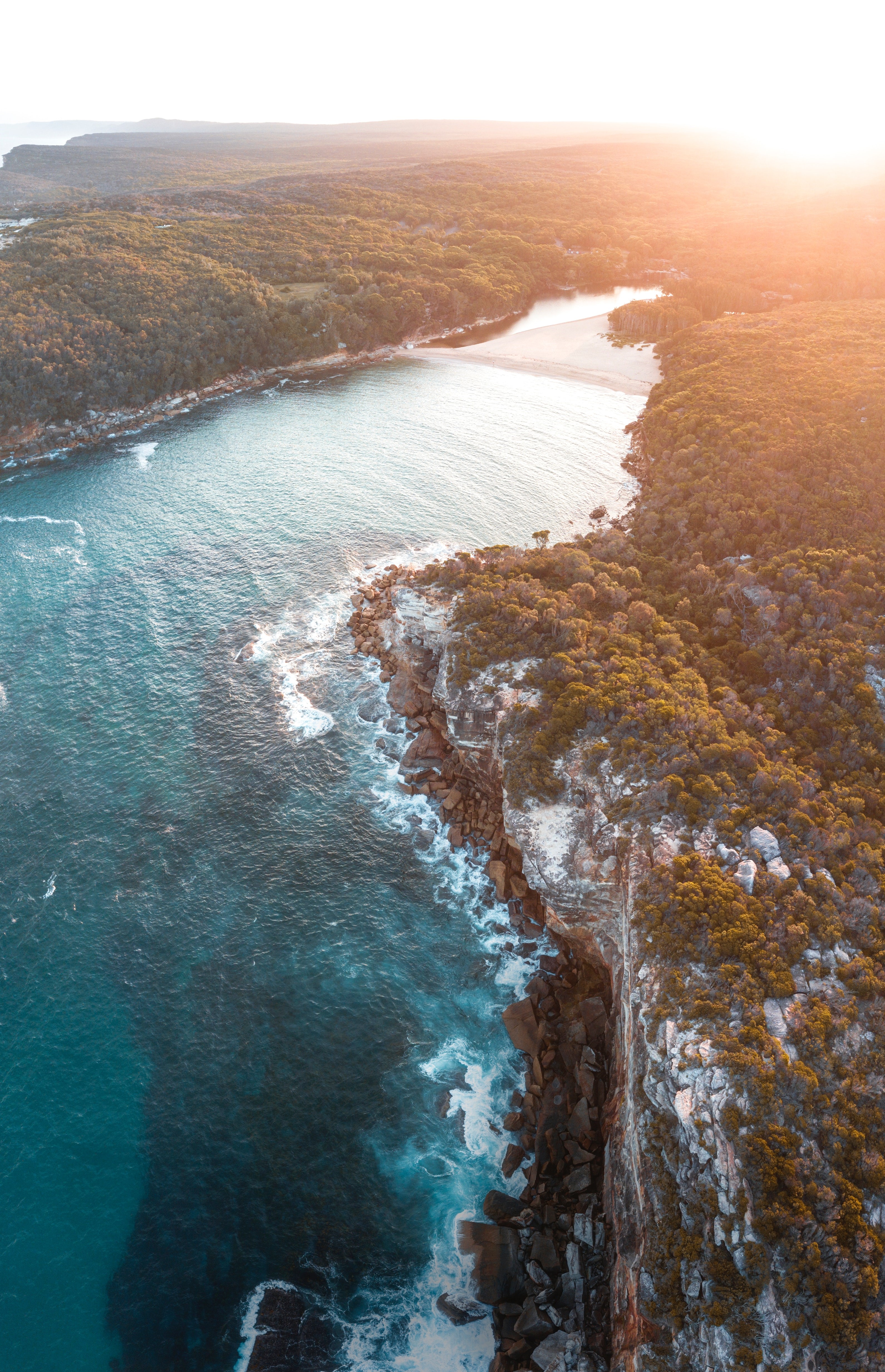 Aerial view of a rugged coastline with a sandy cove HD Phone Wallpaper
