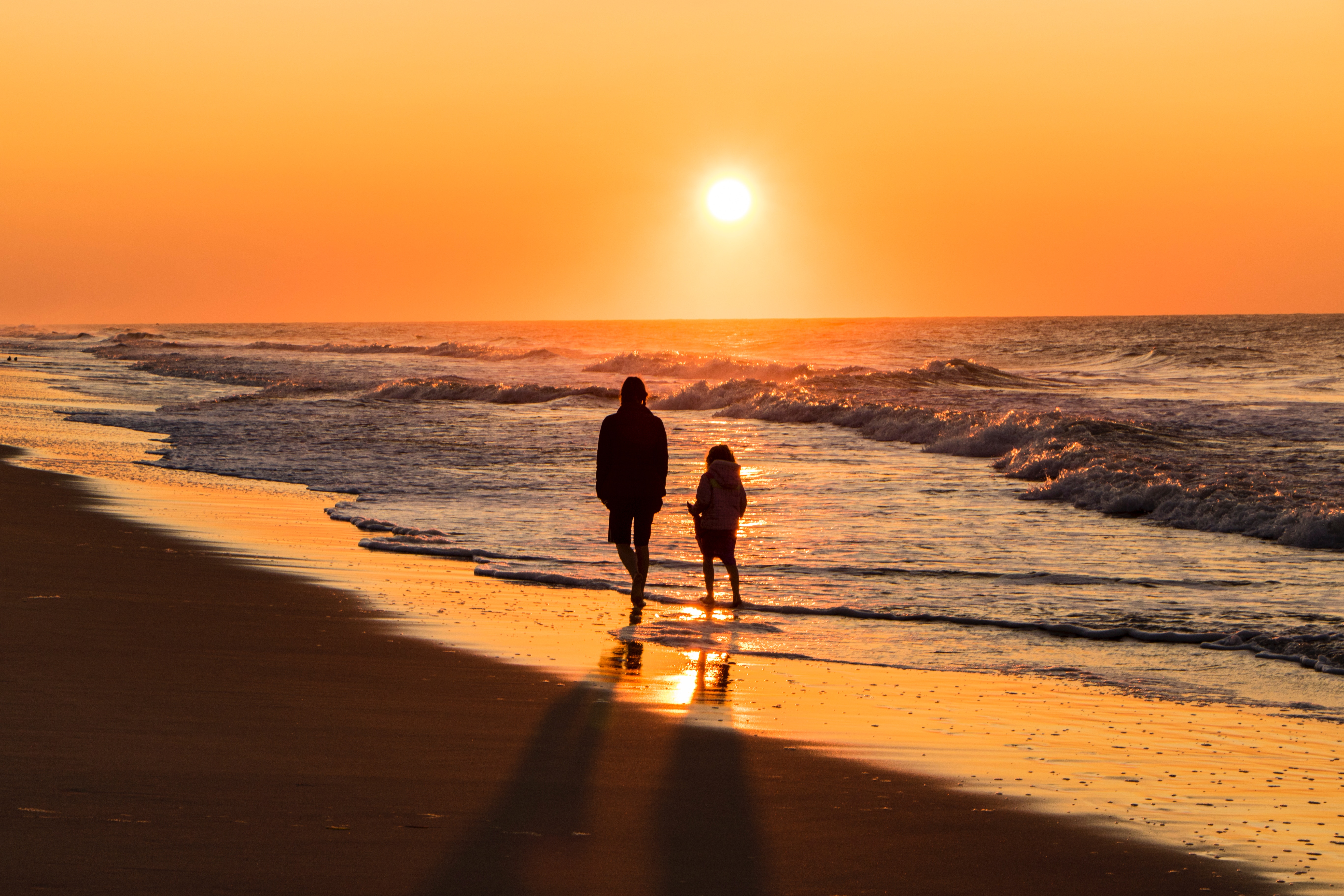 Two people walking on a beach at sunset HD Wallpaper