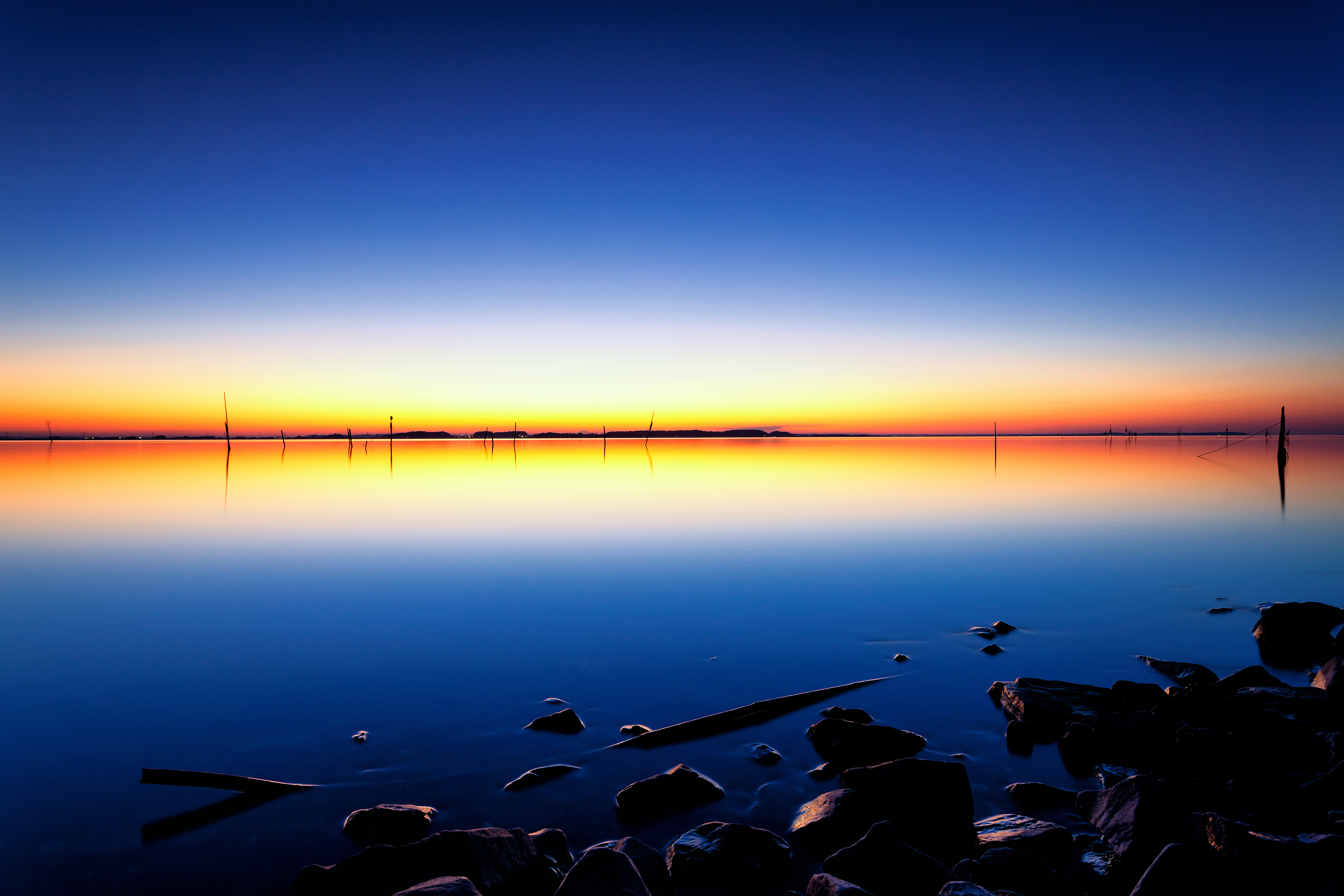 Sunset over a calm lake with rocks in the foreground HD Wallpaper