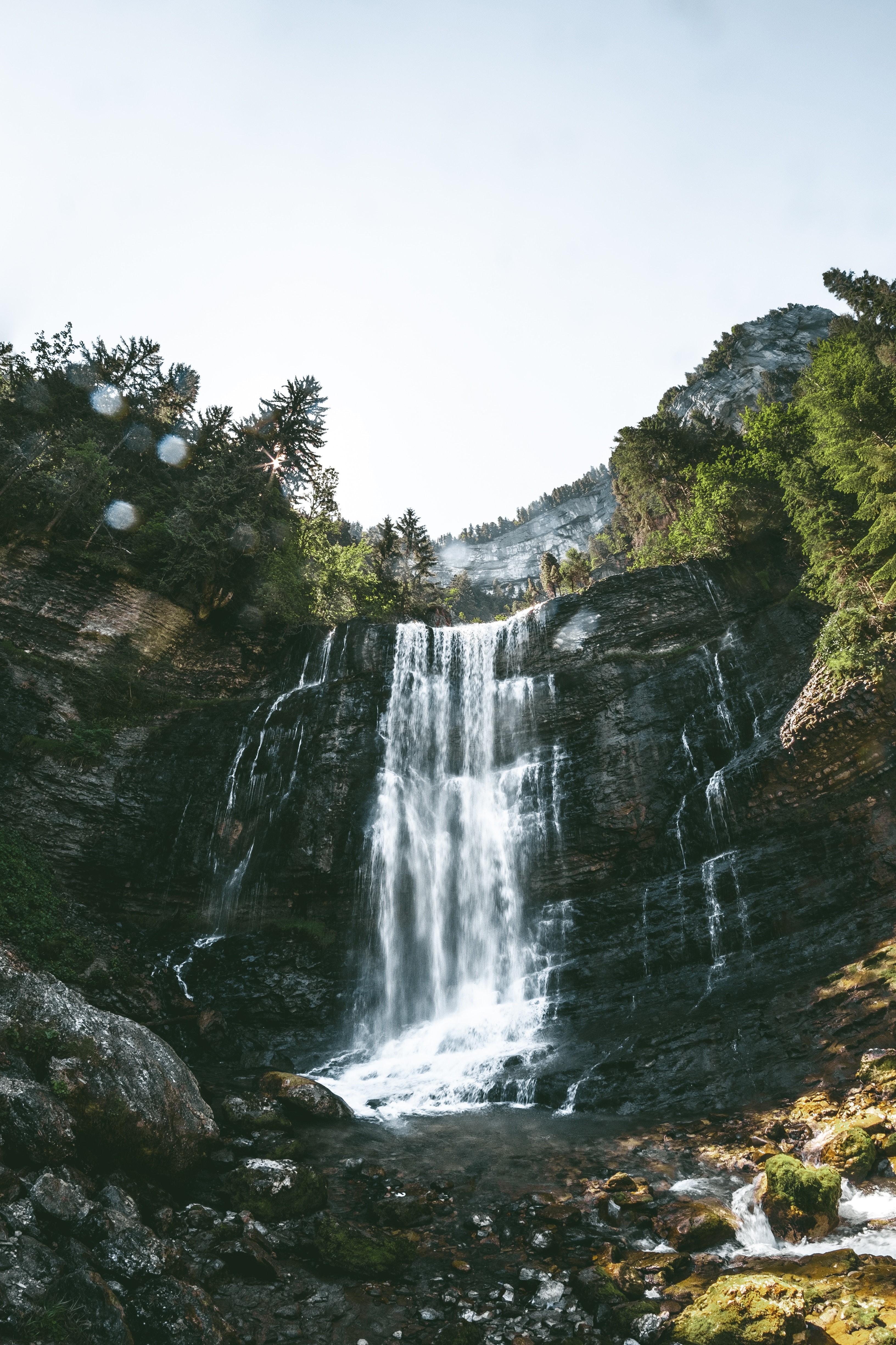 Waterfall cascading down a rocky cliff surrounded by trees HD Phone Wallpaper