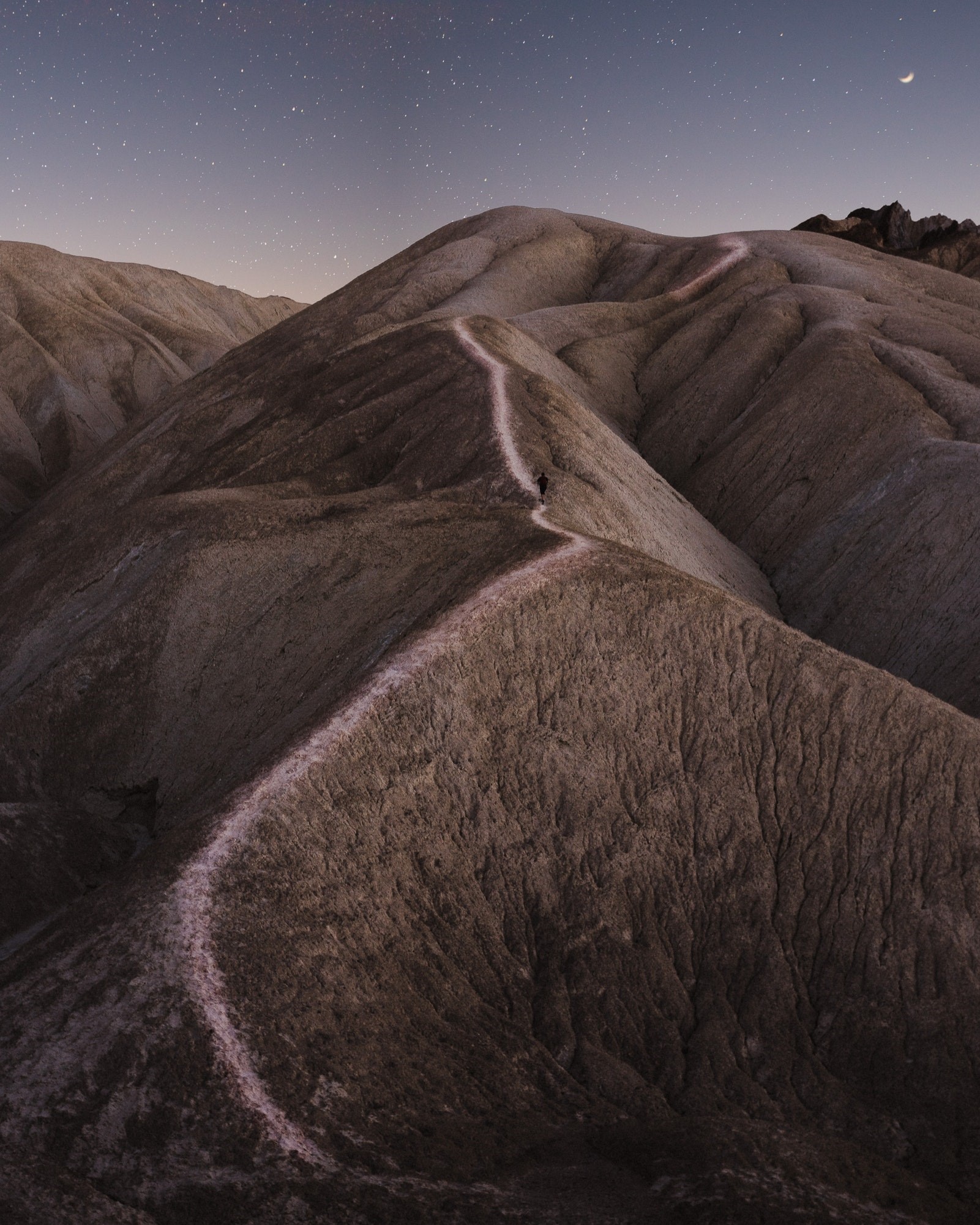 Person walking on a path through hills under the night sky HD Phone Wallpaper