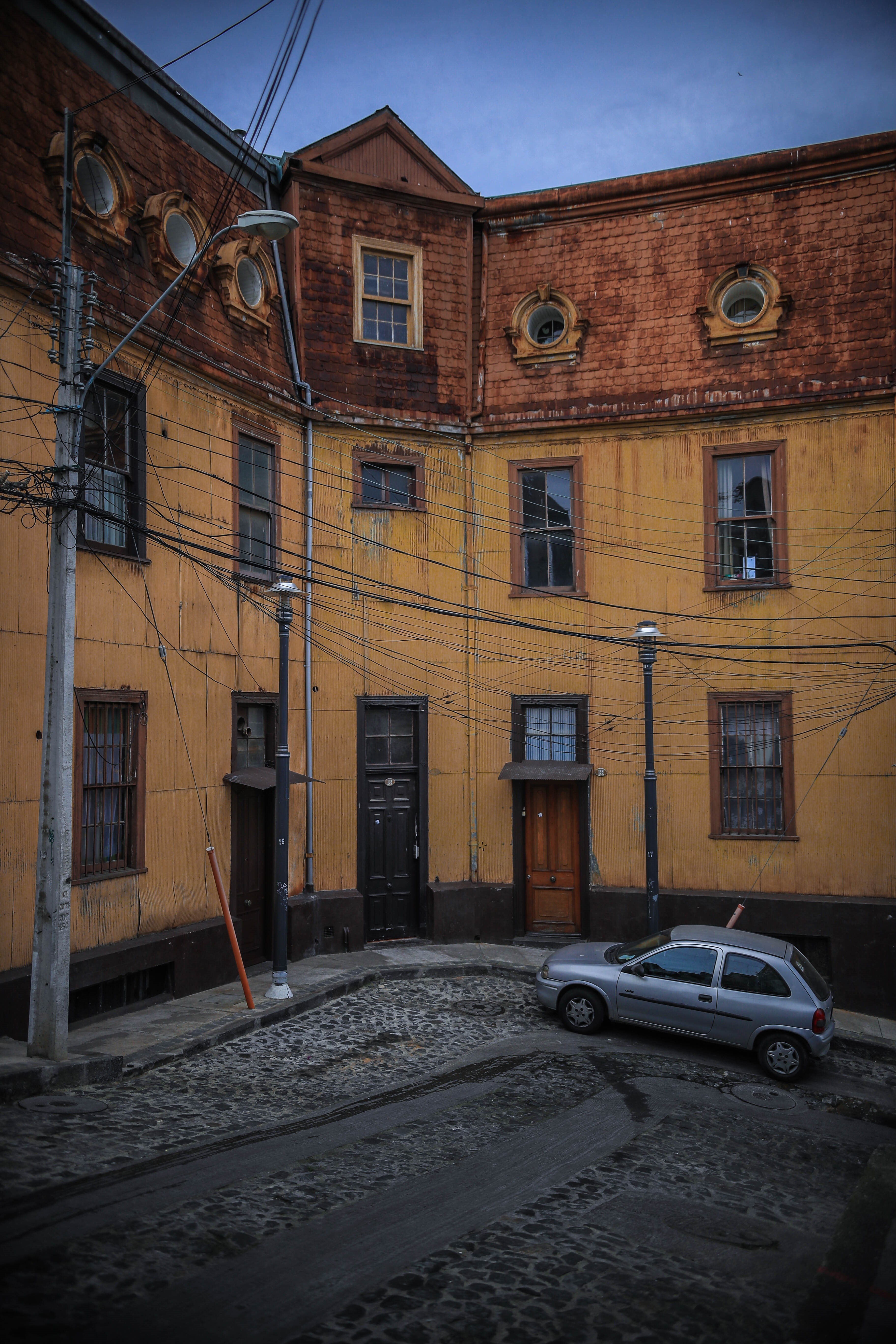 Silver car parked on a cobblestone street in front of a yellow building HD Phone Wallpaper