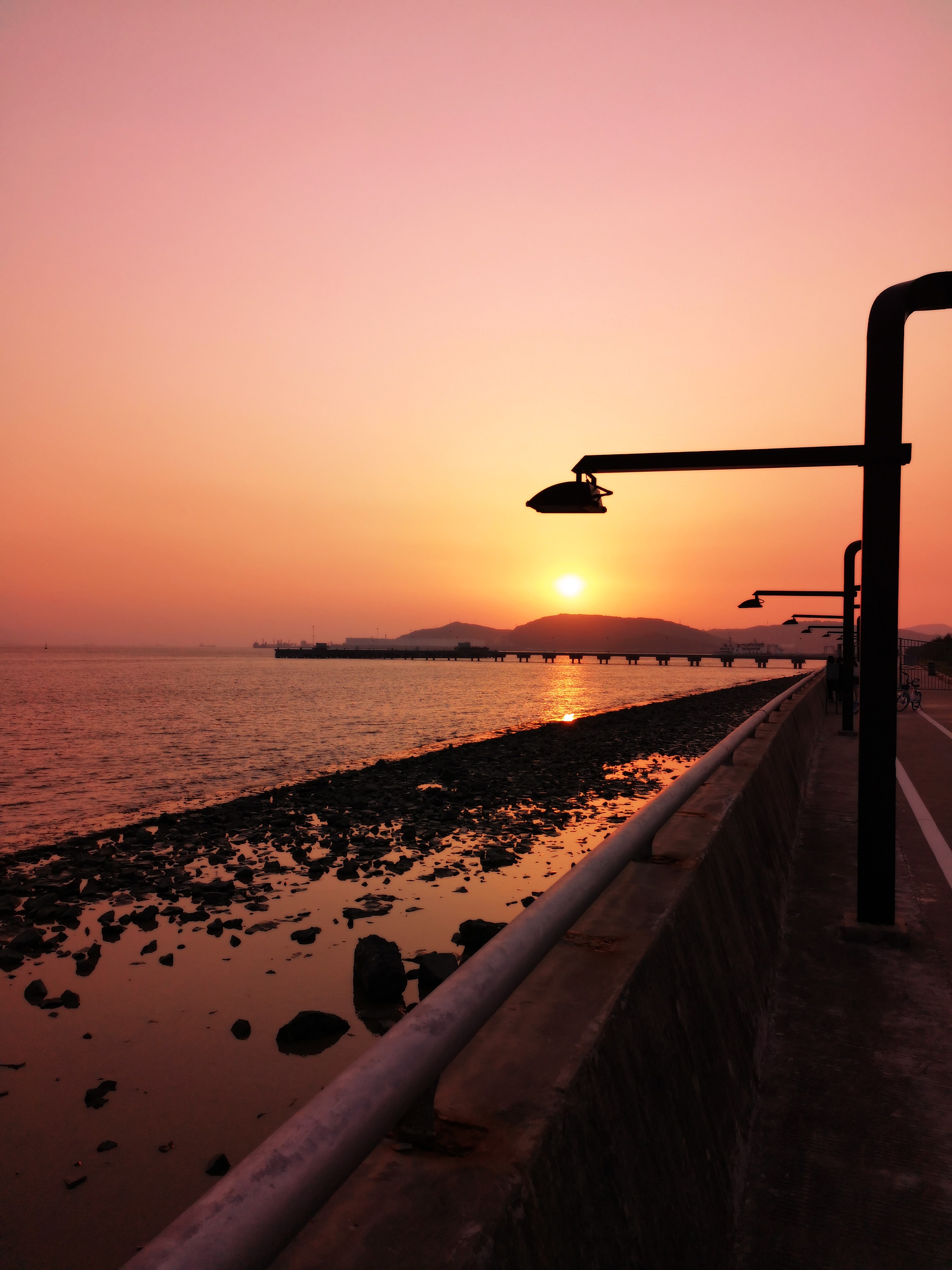 Sunset over the sea with a pier and streetlights HD Phone Wallpaper