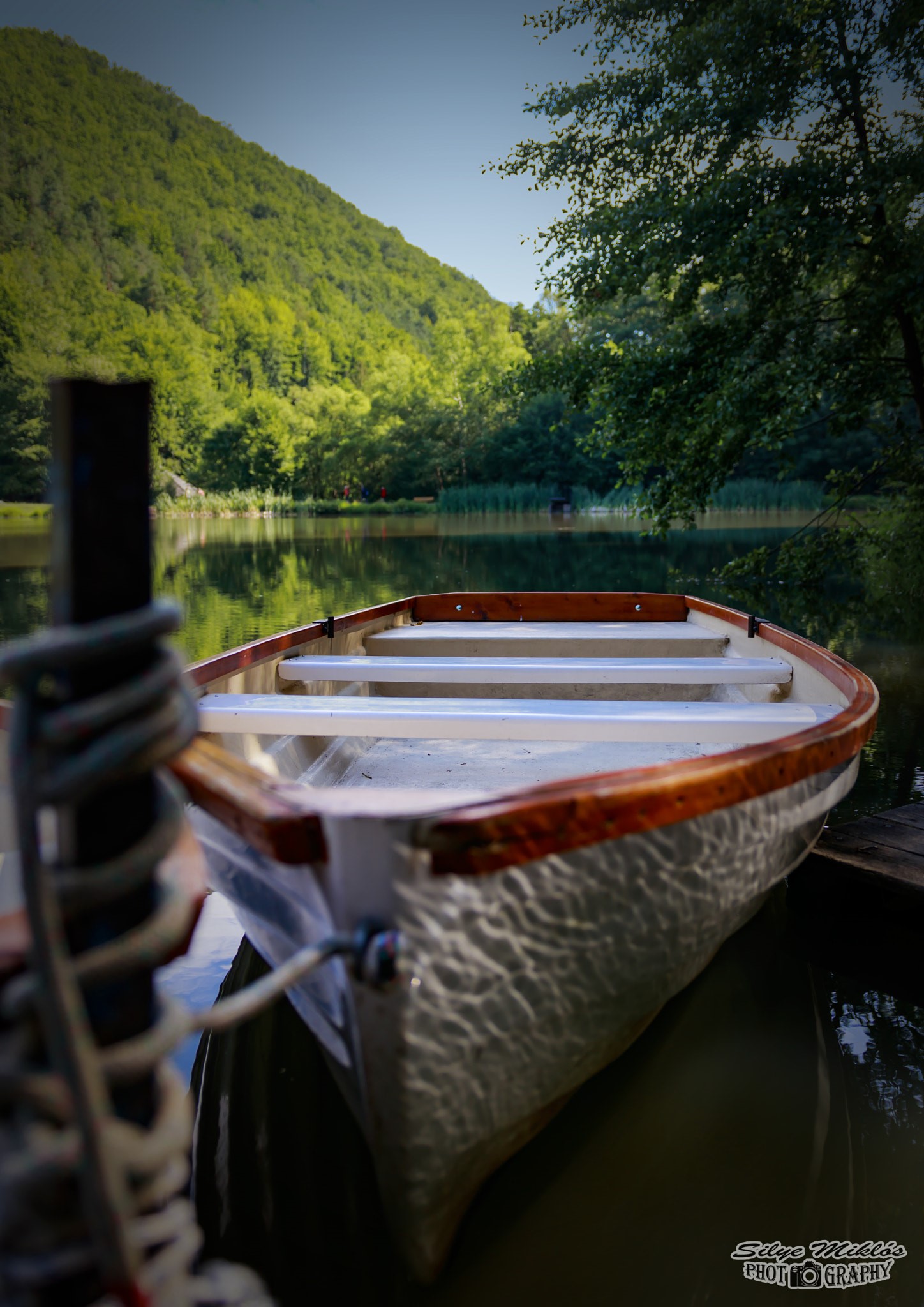 Rowboat docked on a calm lake with forested hills HD Phone Wallpaper