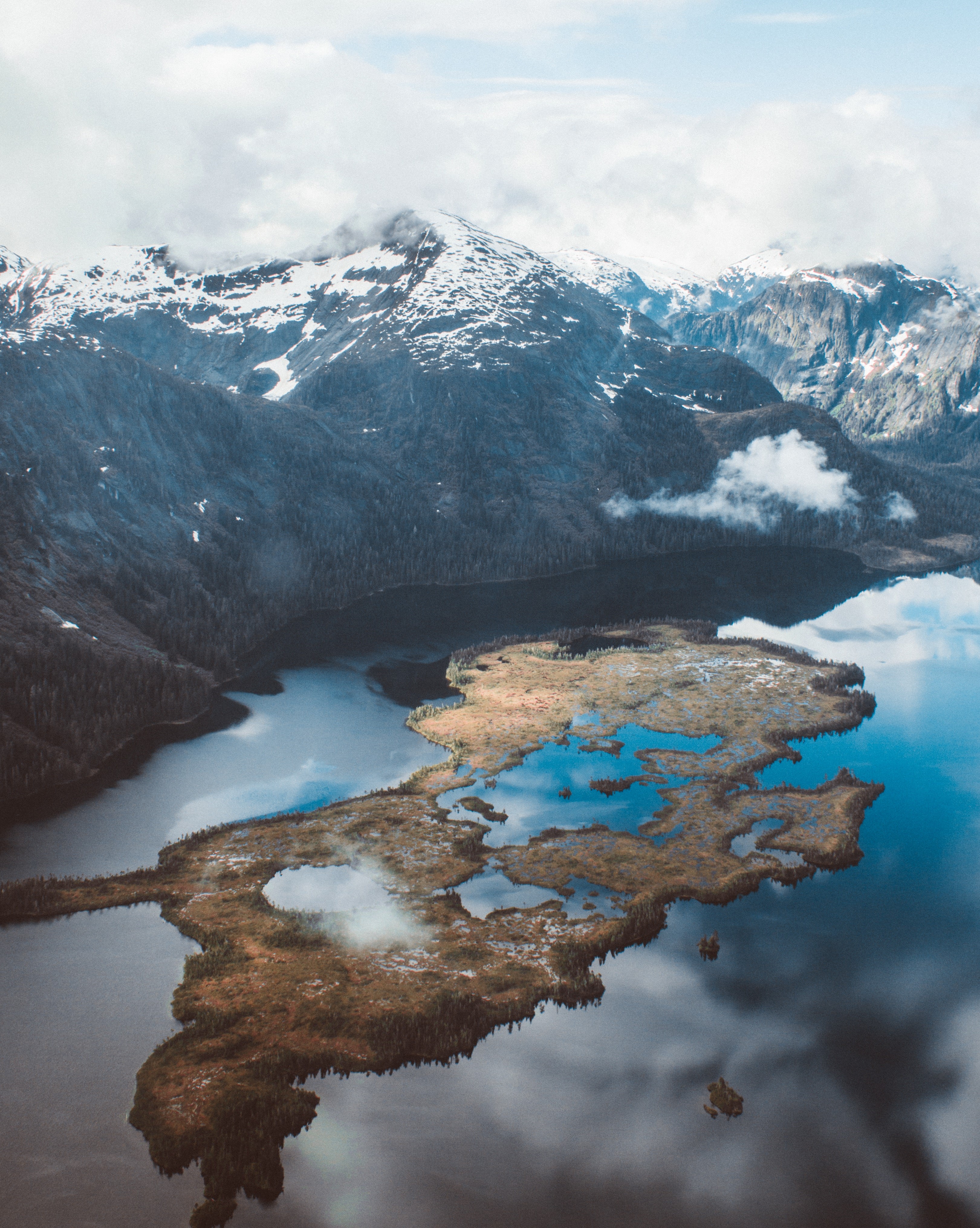 Aerial view of a lake with a snow-capped mountain range HD Phone Wallpaper