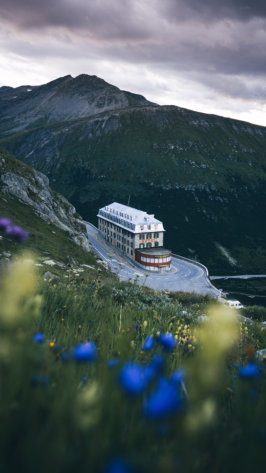 Hotel on a mountain road with flowers in the foreground HD Phone Wallpaper