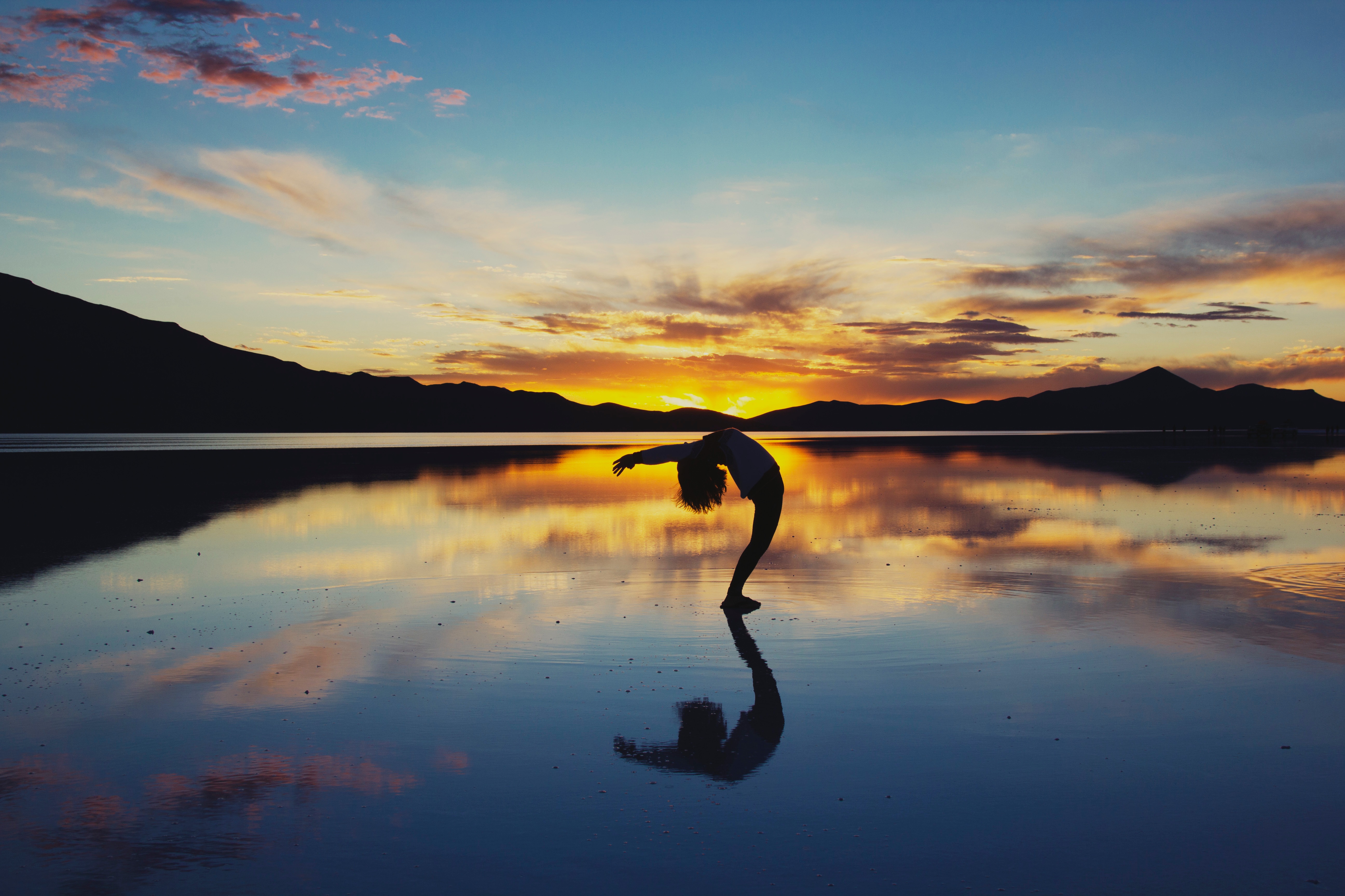 Silhouette of a person doing a backbend at sunset over a reflective body of water HD Wallpaper