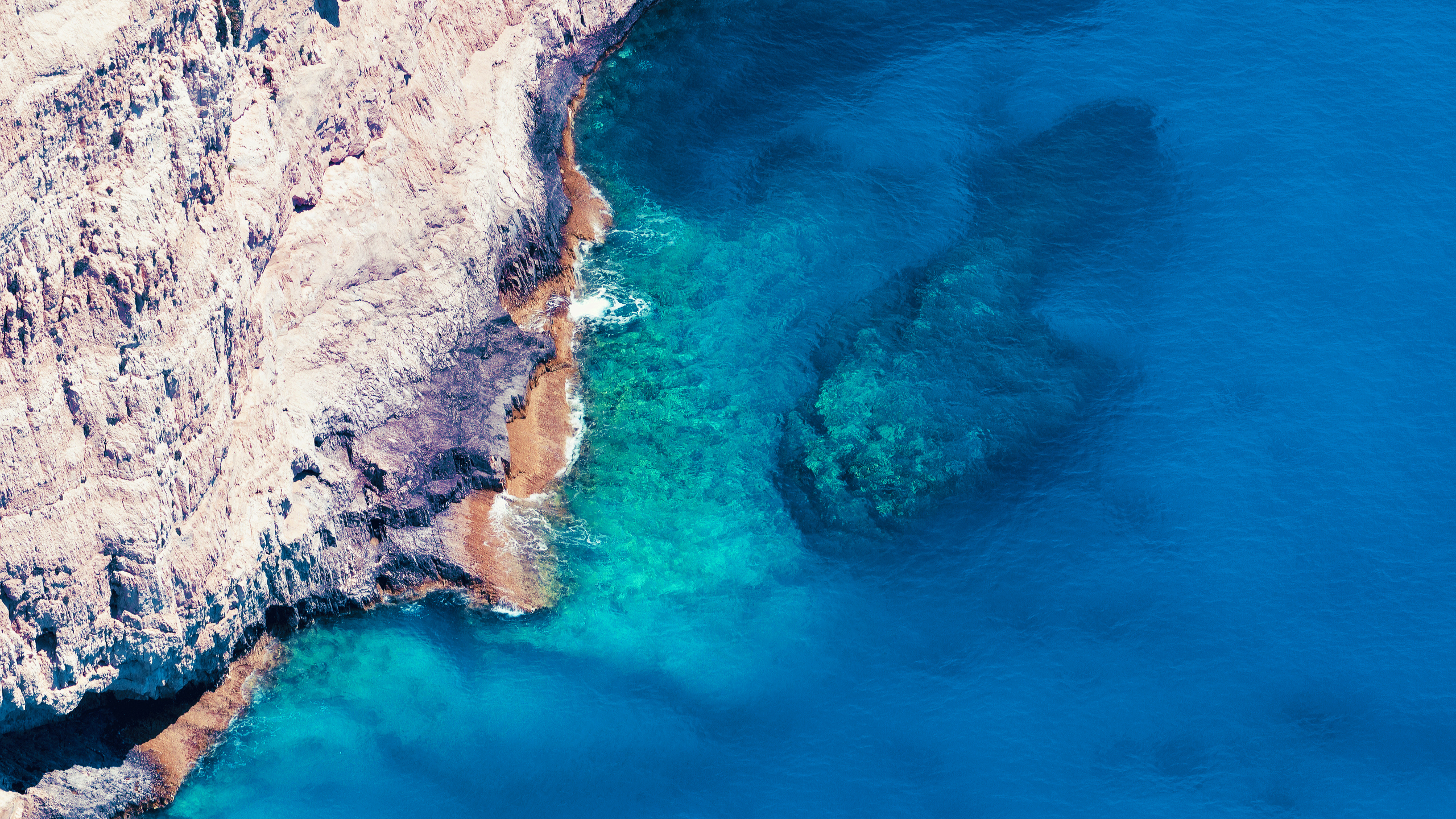 Aerial view of a rocky cliff meeting turquoise and deep blue ocean water HD Wallpaper