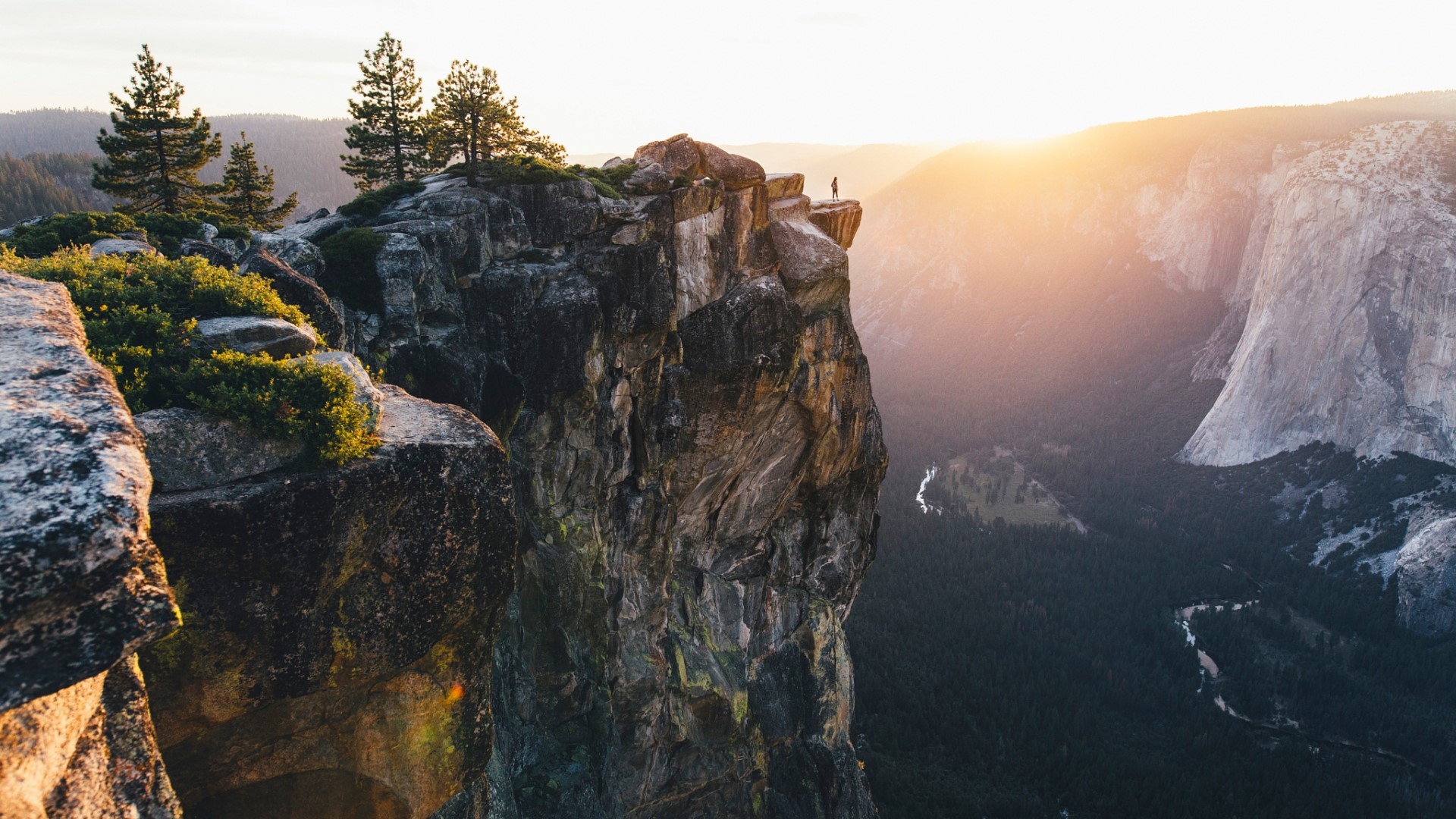 Person standing on a cliff edge at sunset HD Wallpaper