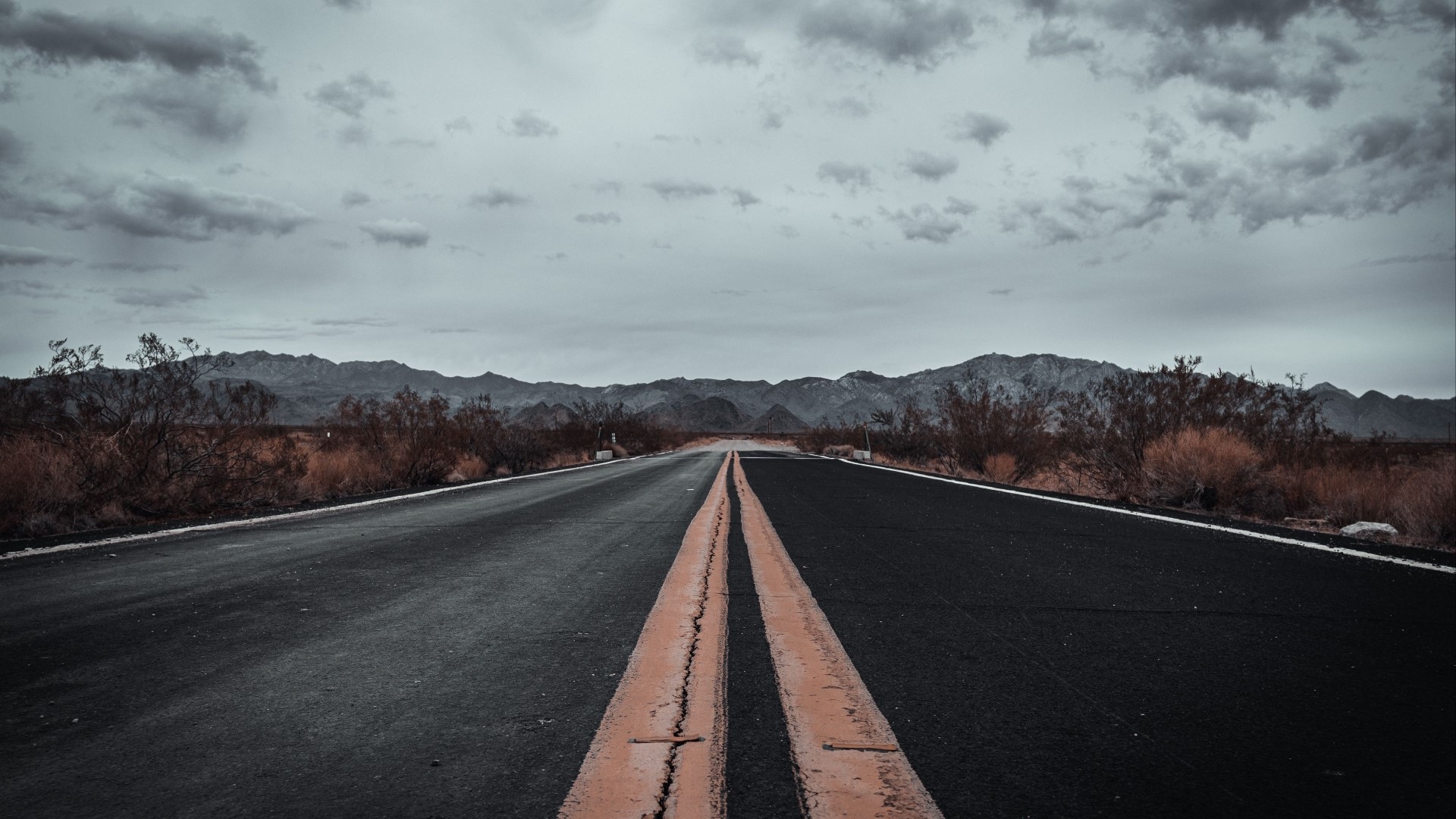 Desert road with mountains under cloudy sky HD Wallpaper