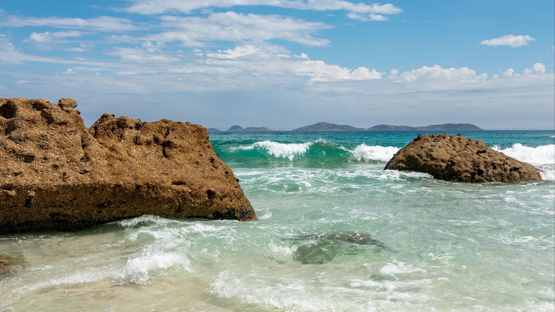 Rocky shore with waves and distant islands HD Wallpaper