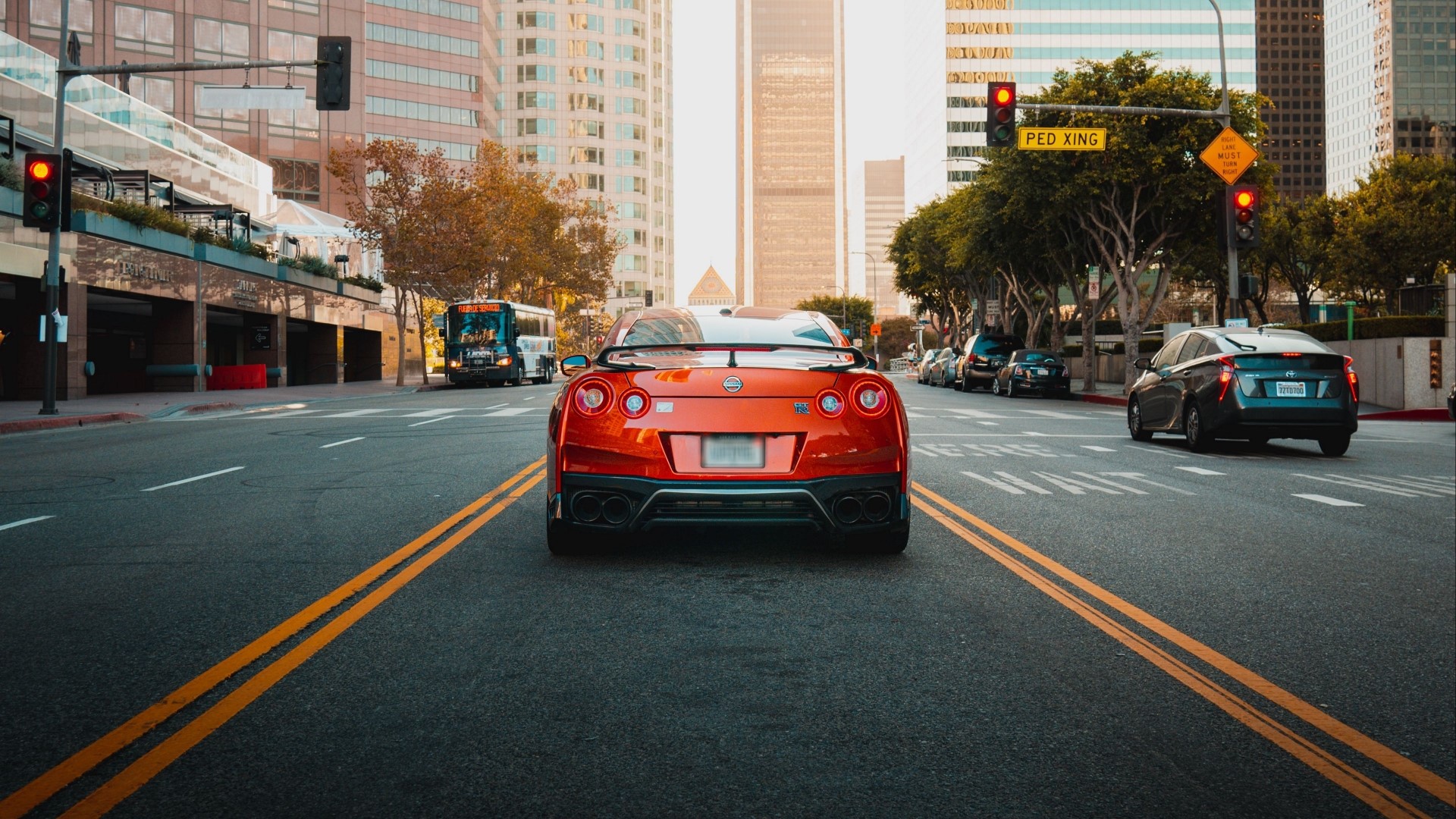 Orange Nissan GT-R driving on a city street HD Wallpaper