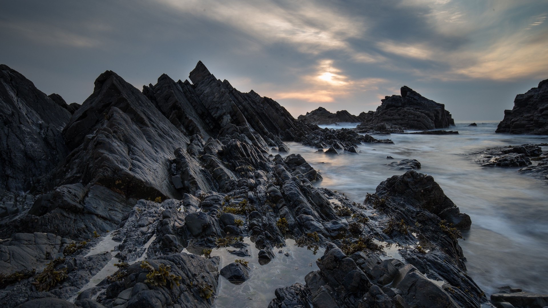 Jagged dark rocks on a rocky coast with ocean waves HD Wallpaper