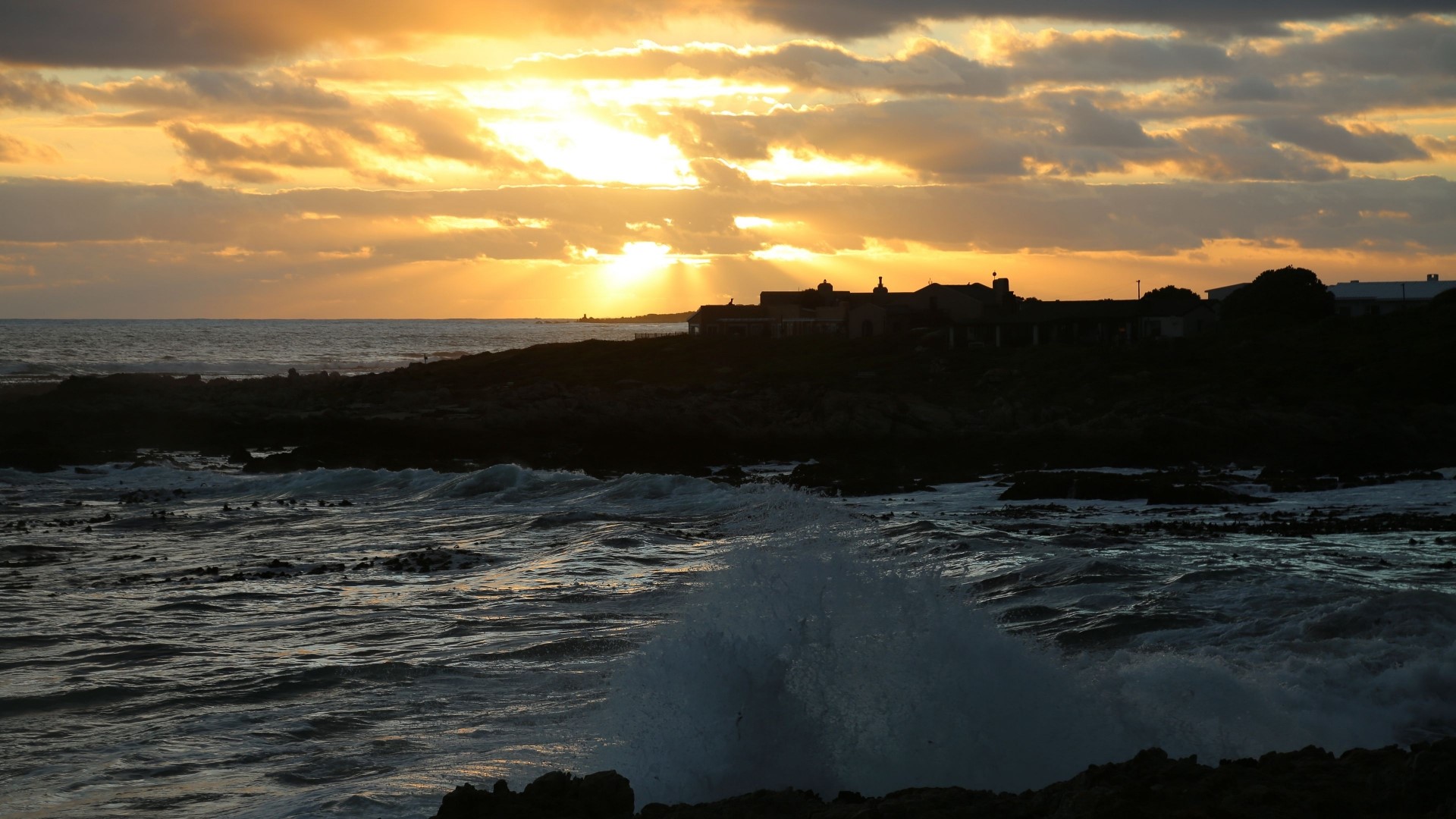 Sunset over the ocean with waves crashing on rocks HD Wallpaper