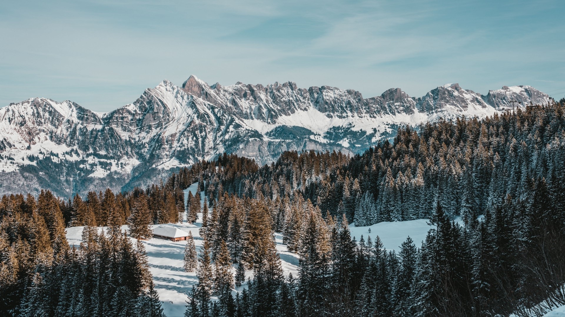 Snowy mountains and forest with a cabin HD Wallpaper