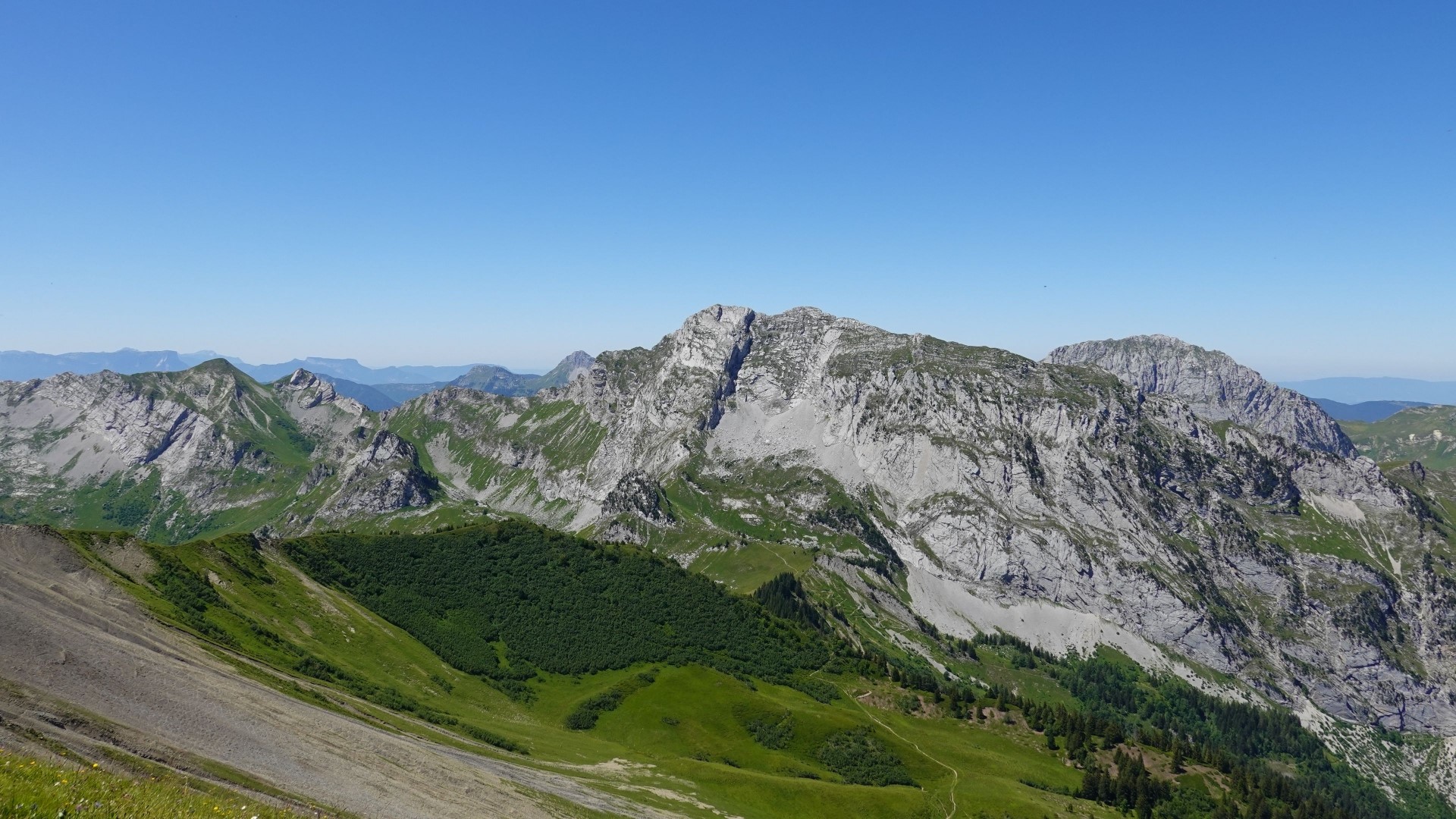 Rocky mountains with green slopes under a clear blue sky HD Wallpaper