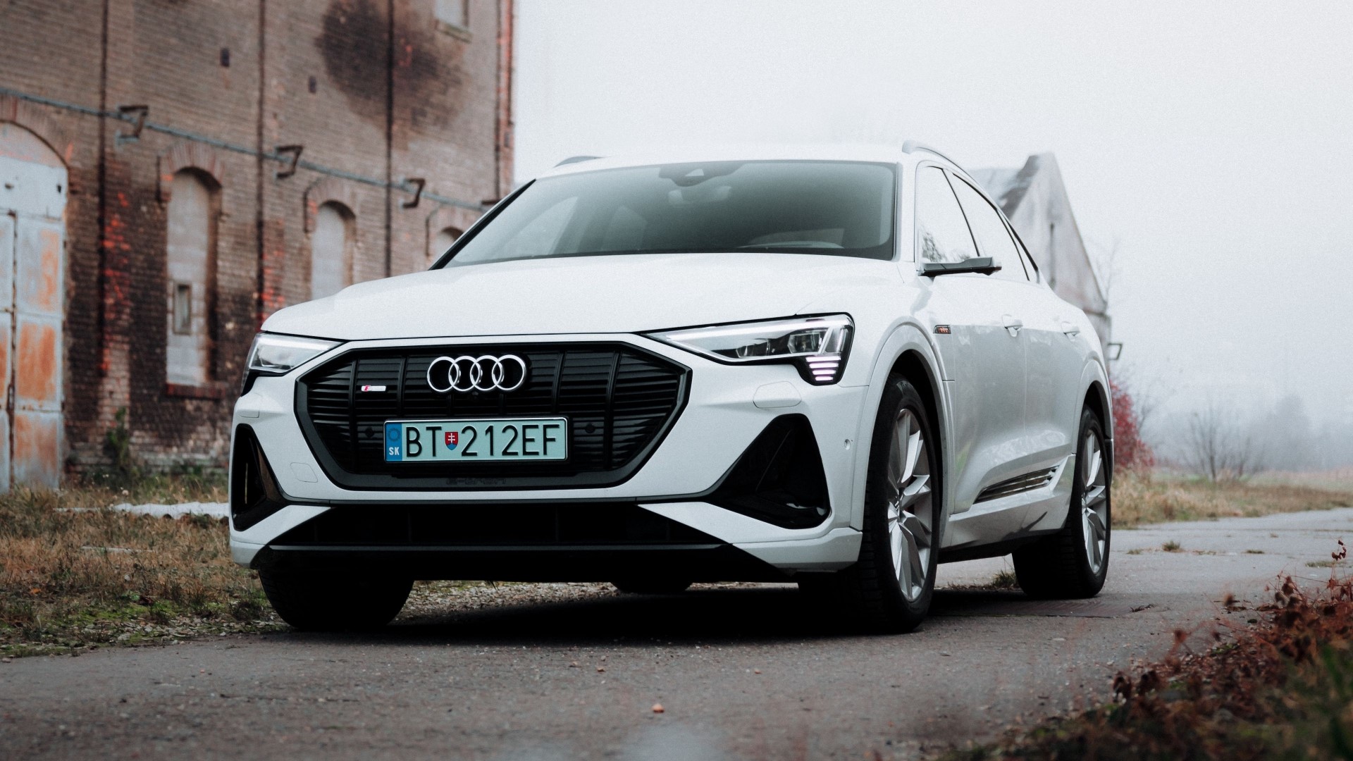 White Audi e-tron parked near a brick building HD Wallpaper